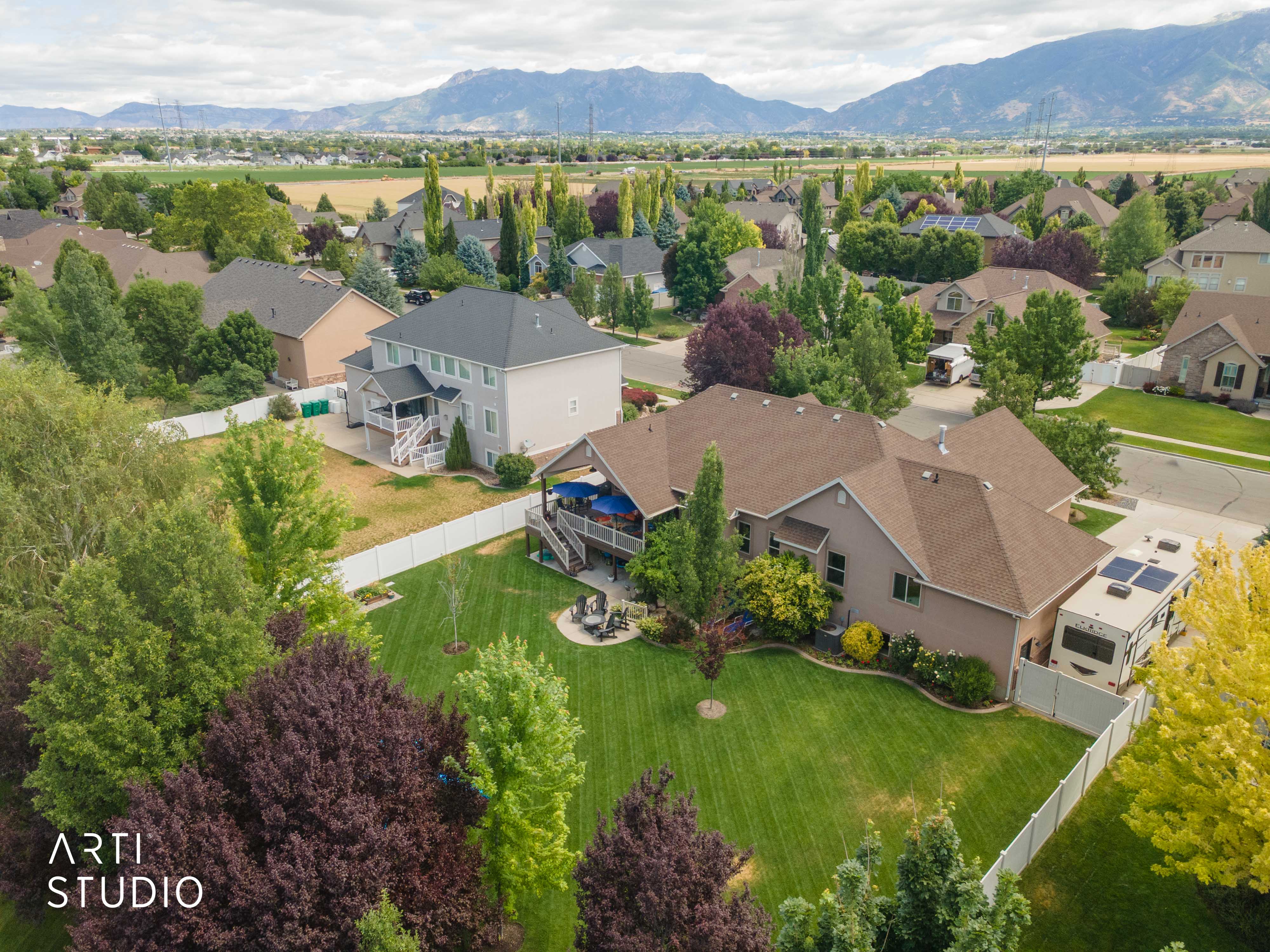 Expansive property featuring a verdant lawn, mature landscaping, large covered deck, concrete fire pit area, and fully fenced backyard