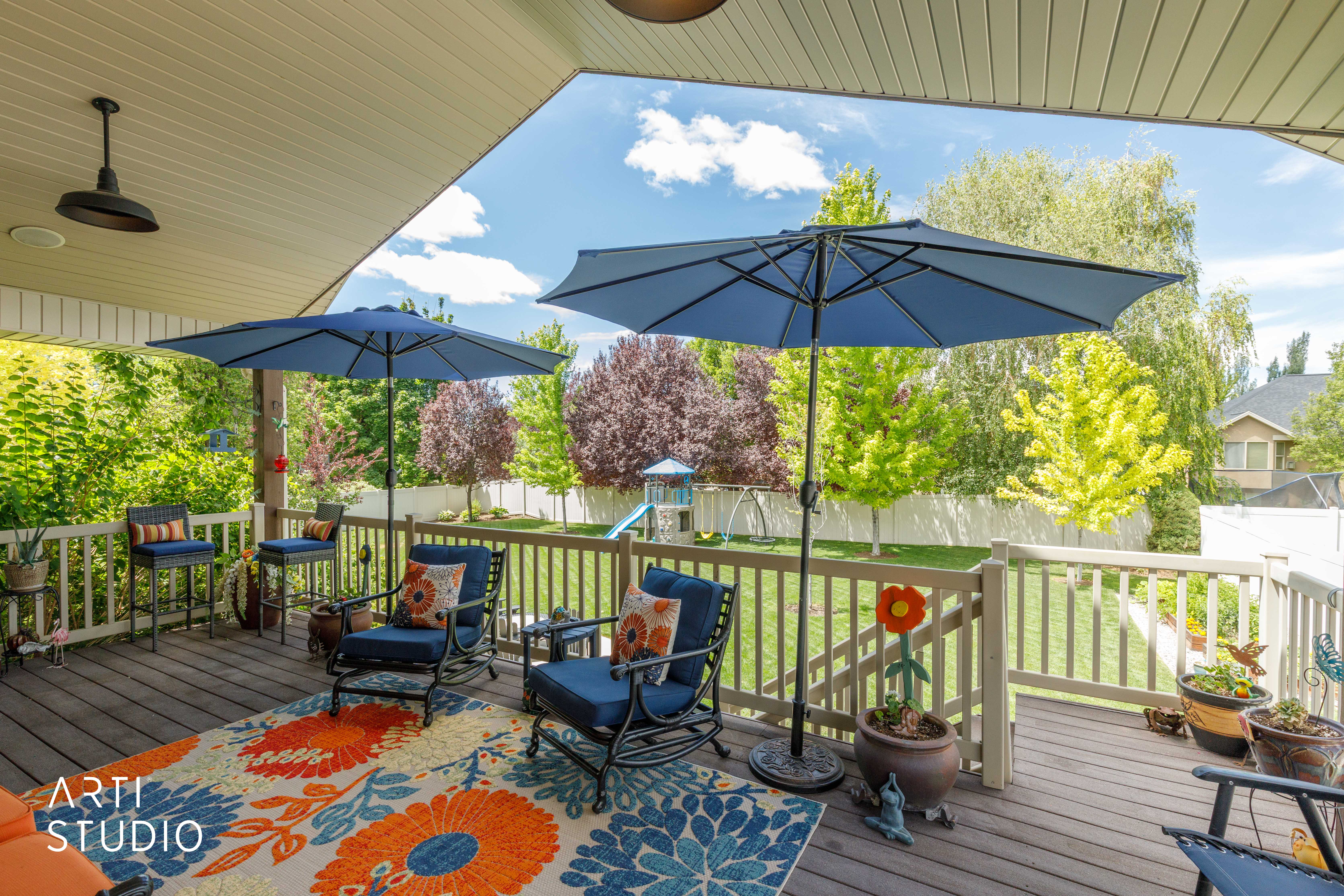 Spacious wooden deck featuring a covered area with a ceiling-mounted light fixture, white railing, and a vibrant green yard beyond