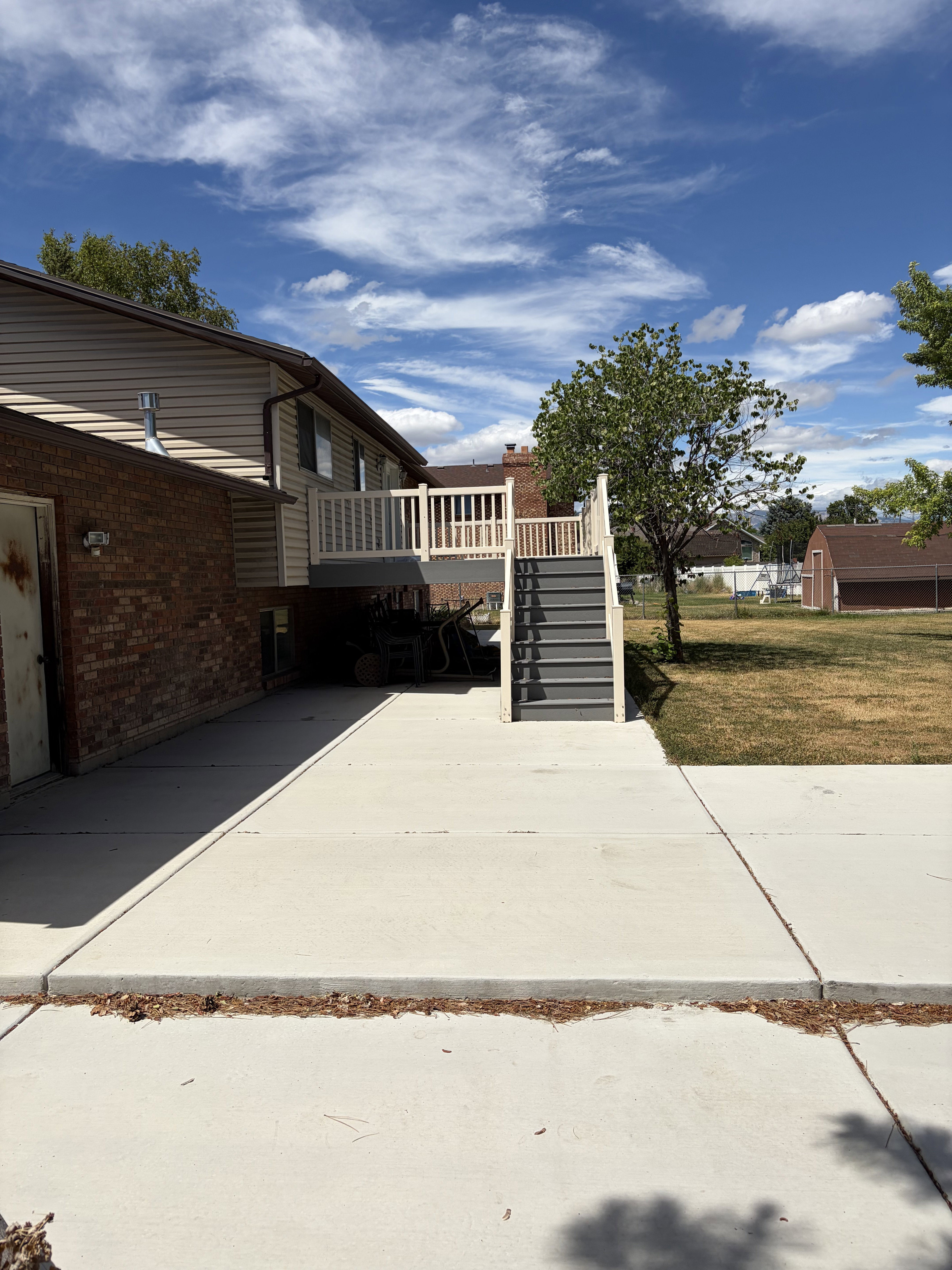 Rear exterior featuring a spacious concrete patio, multi-level deck with white railings, and a wide staircase