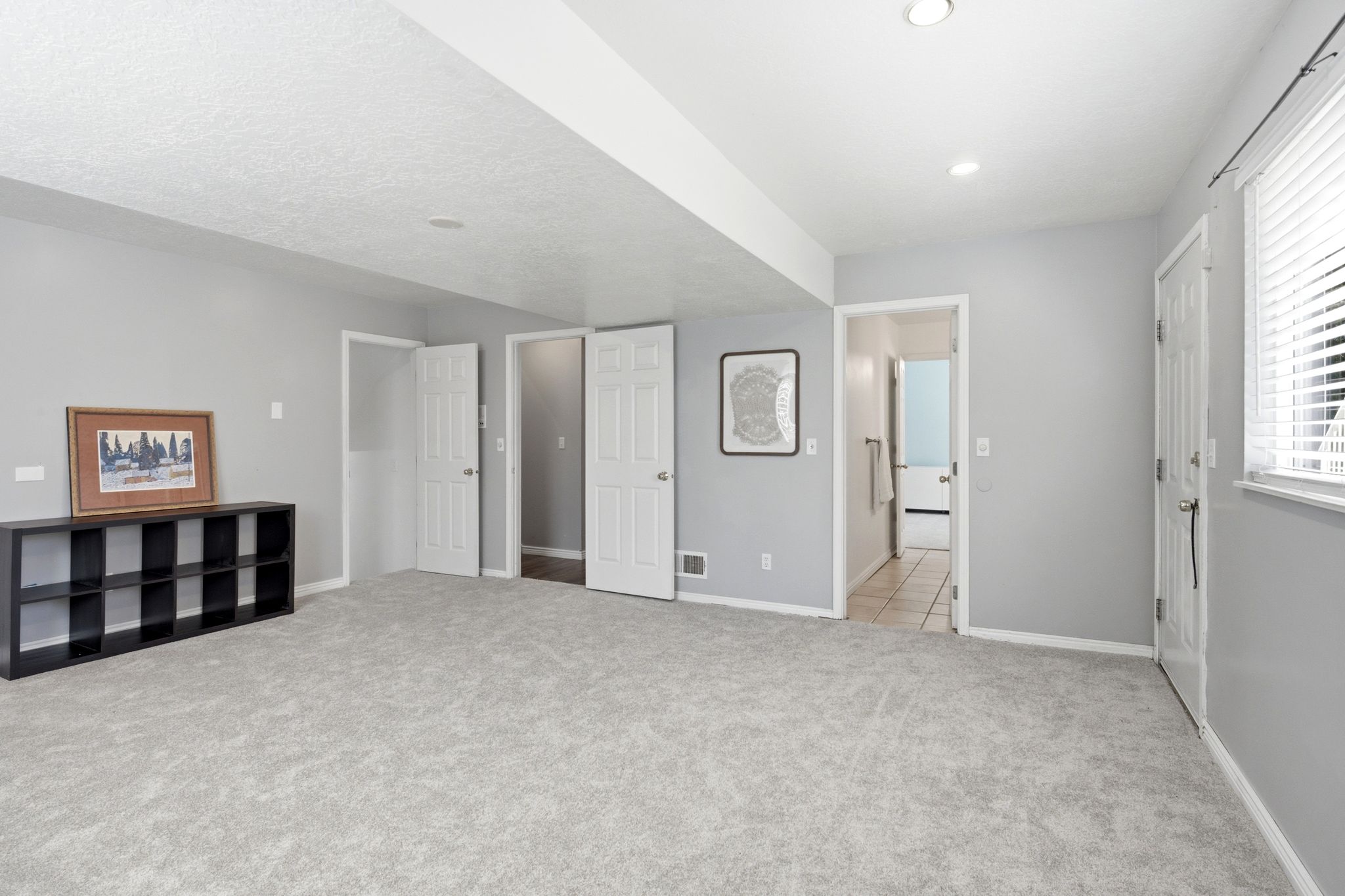 Spacious room featuring light gray carpet flooring, recessed lighting, and a window with horizontal blinds
