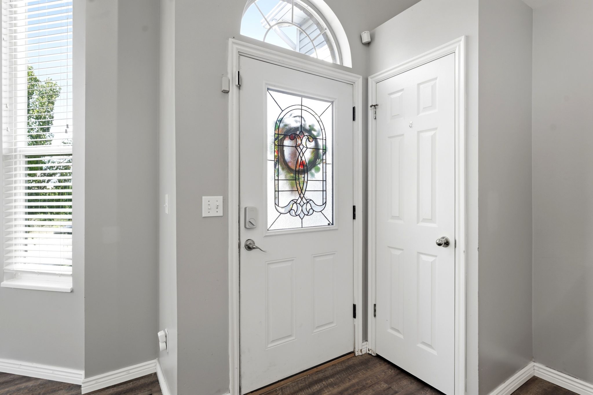 Entryway featuring a decorative glass panel door with an arched transom window, wood-finish flooring, and light gray wall paint