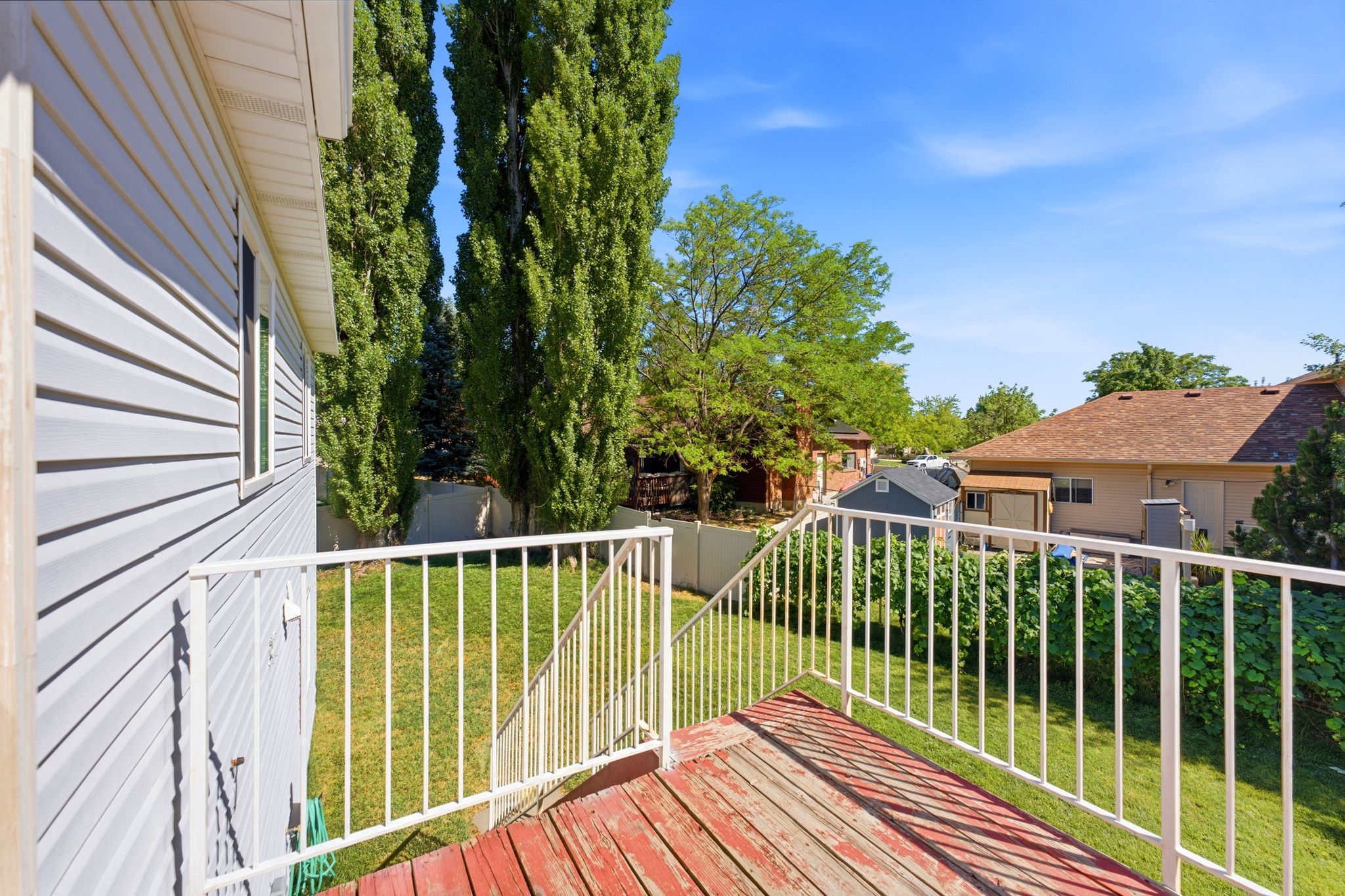 Rear deck with white metal railing, wood-finish decking, and direct access to a grassy yard