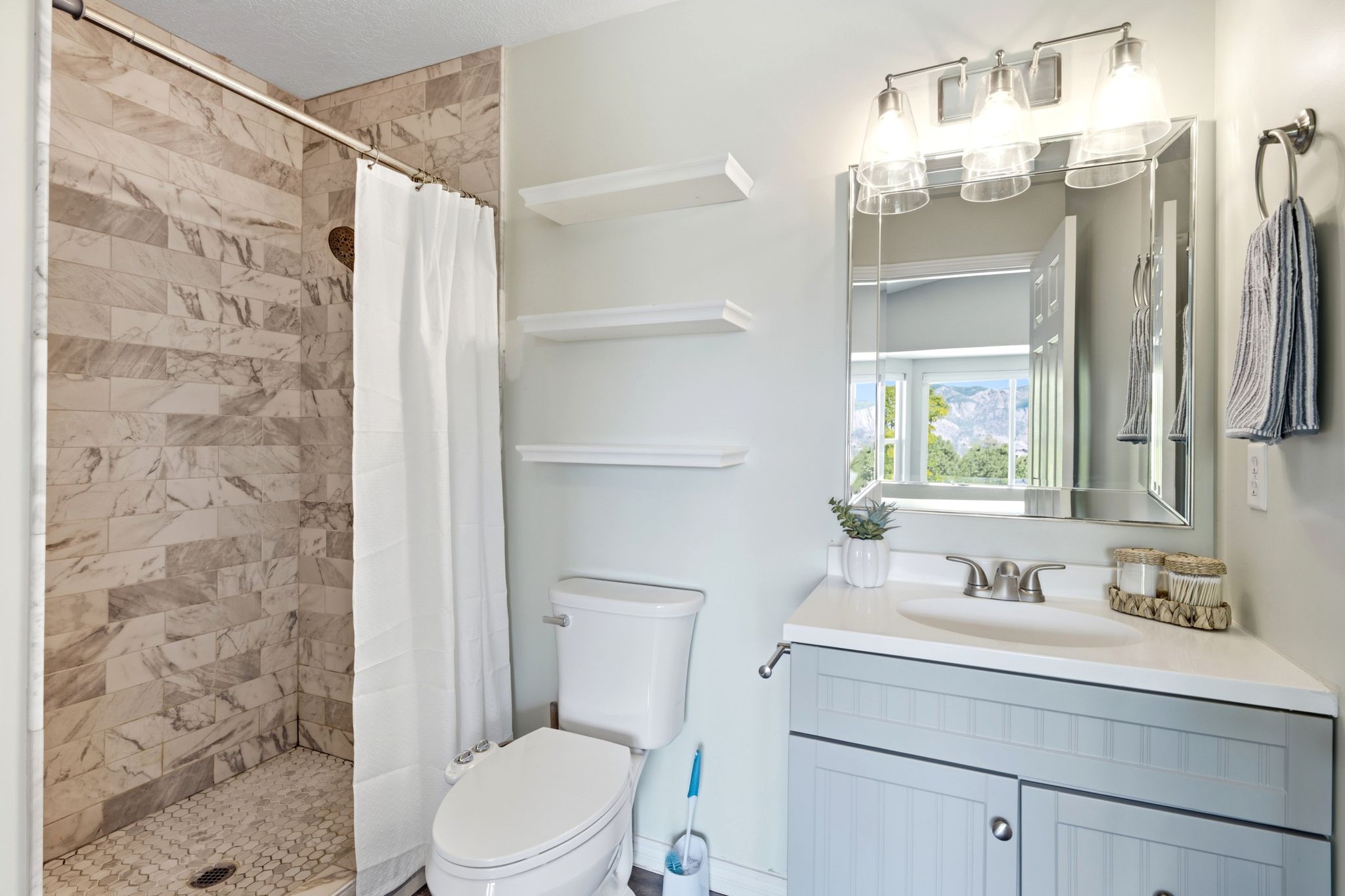 Bathroom featuring a tile shower with a mosaic floor, a single vanity with a light countertop, a framed mirror, and a three-light fixture