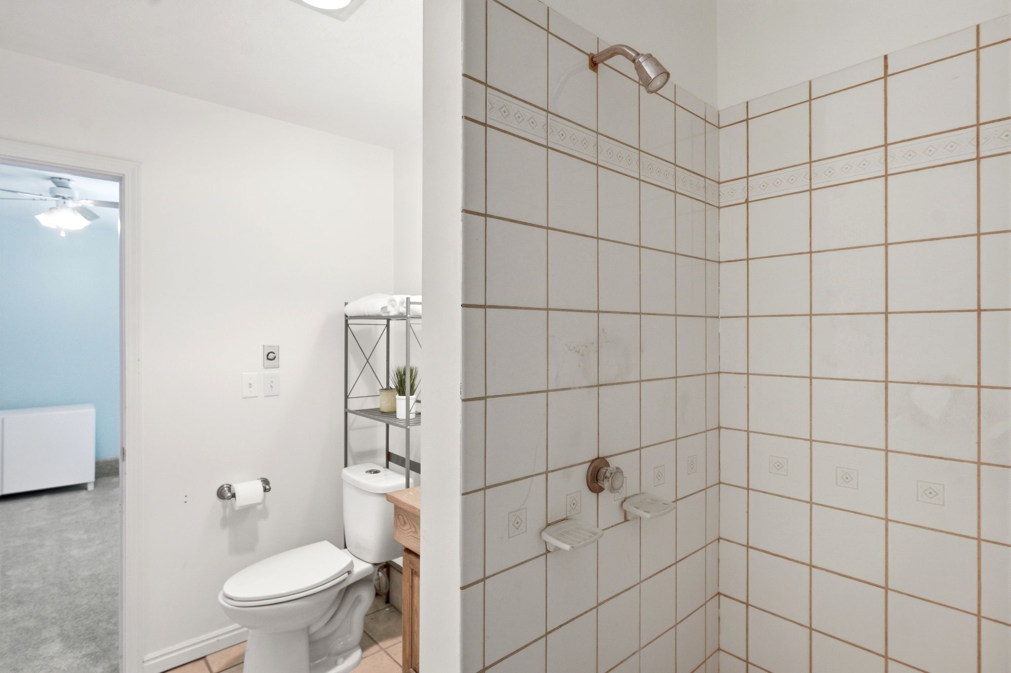 Shower with white ceramic tile surround featuring decorative accent tiles and a bronze-finish shower head