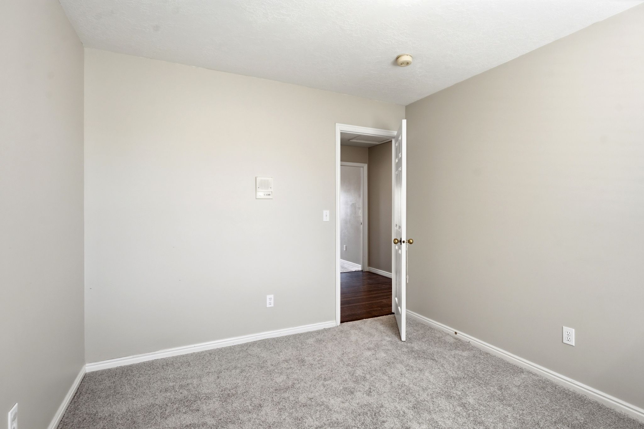 Room featuring light gray wall paint, gray carpeting, white baseboards, and a standard door with a brass knob