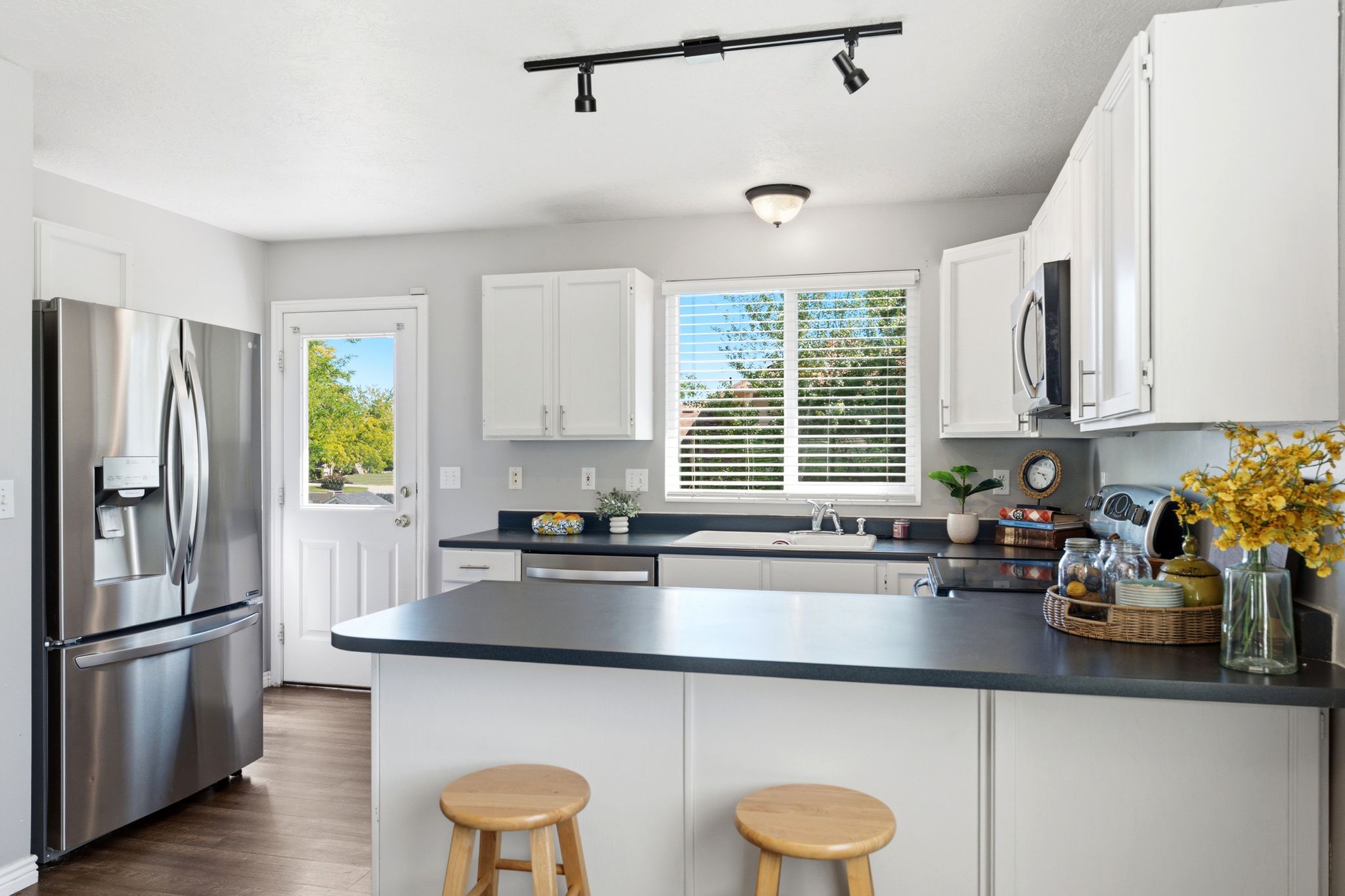 Kitchen featuring white cabinetry, dark countertops, a stainless steel refrigerator, and wood-finish flooring