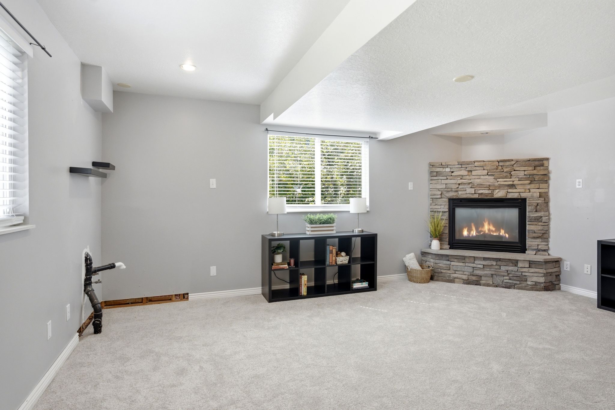 Living area featuring light gray walls, light gray carpet, and a prominent corner fireplace with stacked stone surround