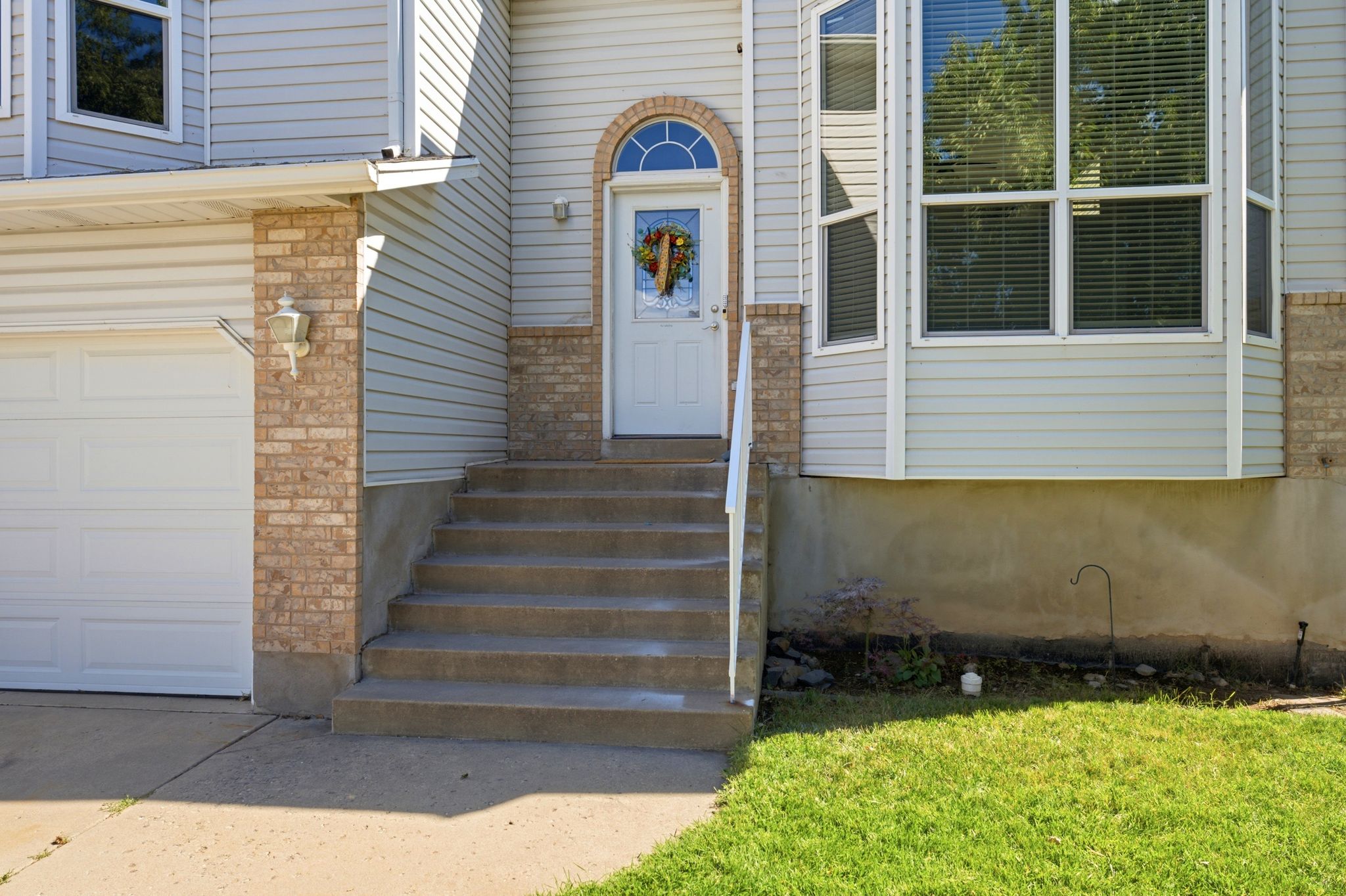 Front exterior featuring a white entry door with an arched transom window, a bay window with blinds, light-colored siding, and brick accents