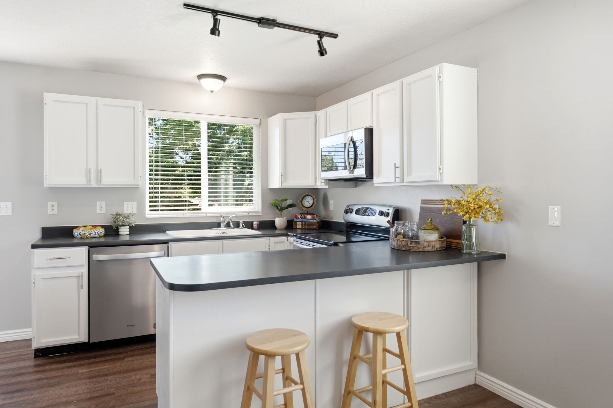 Kitchen featuring white cabinetry, dark countertops, a stainless steel dishwasher, an over-range microwave, and dark wood-finish flooring