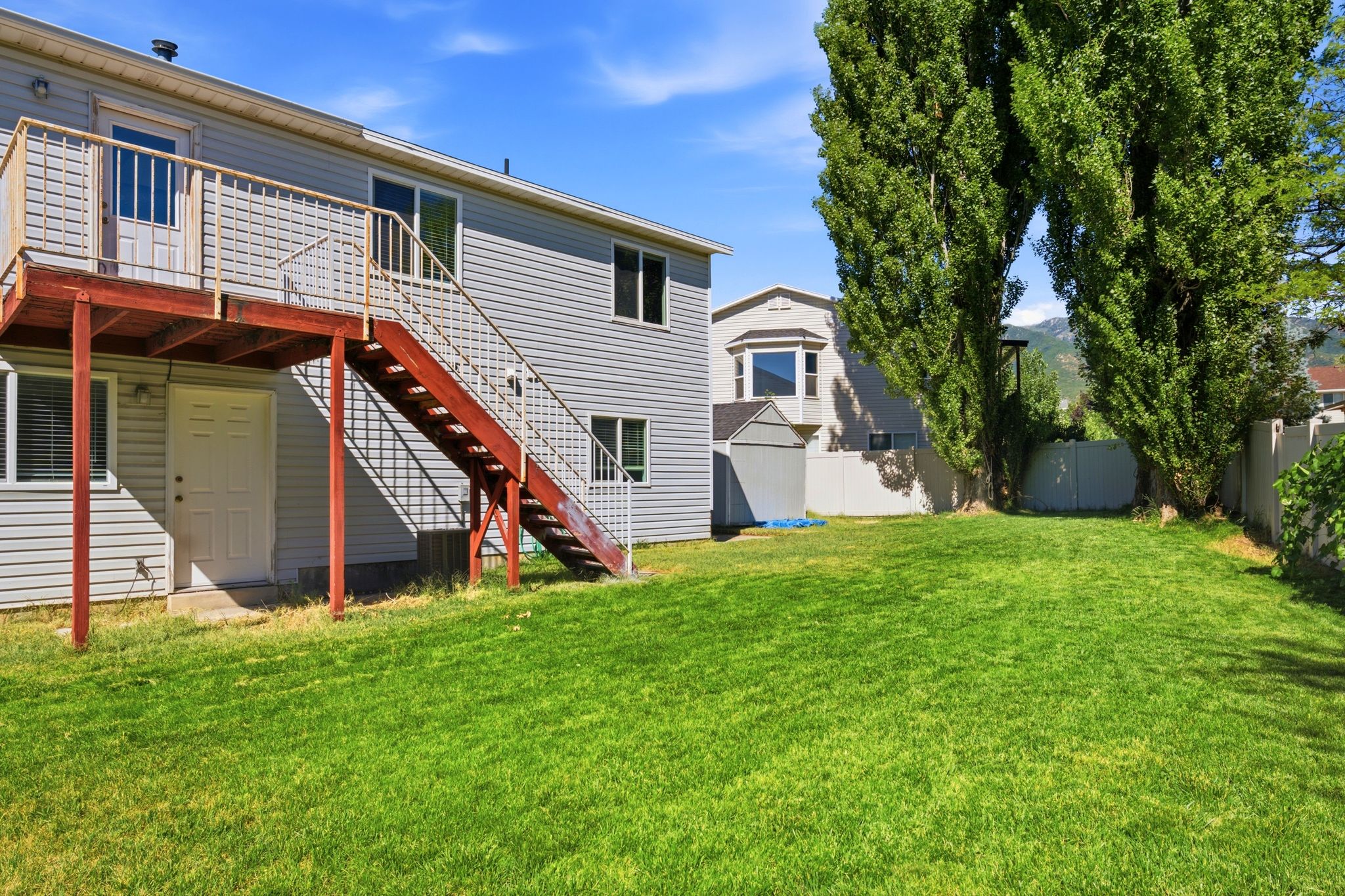Expansive grassy yard featuring a multi-level deck with stairs, a shed, and mature trees along the perimeter