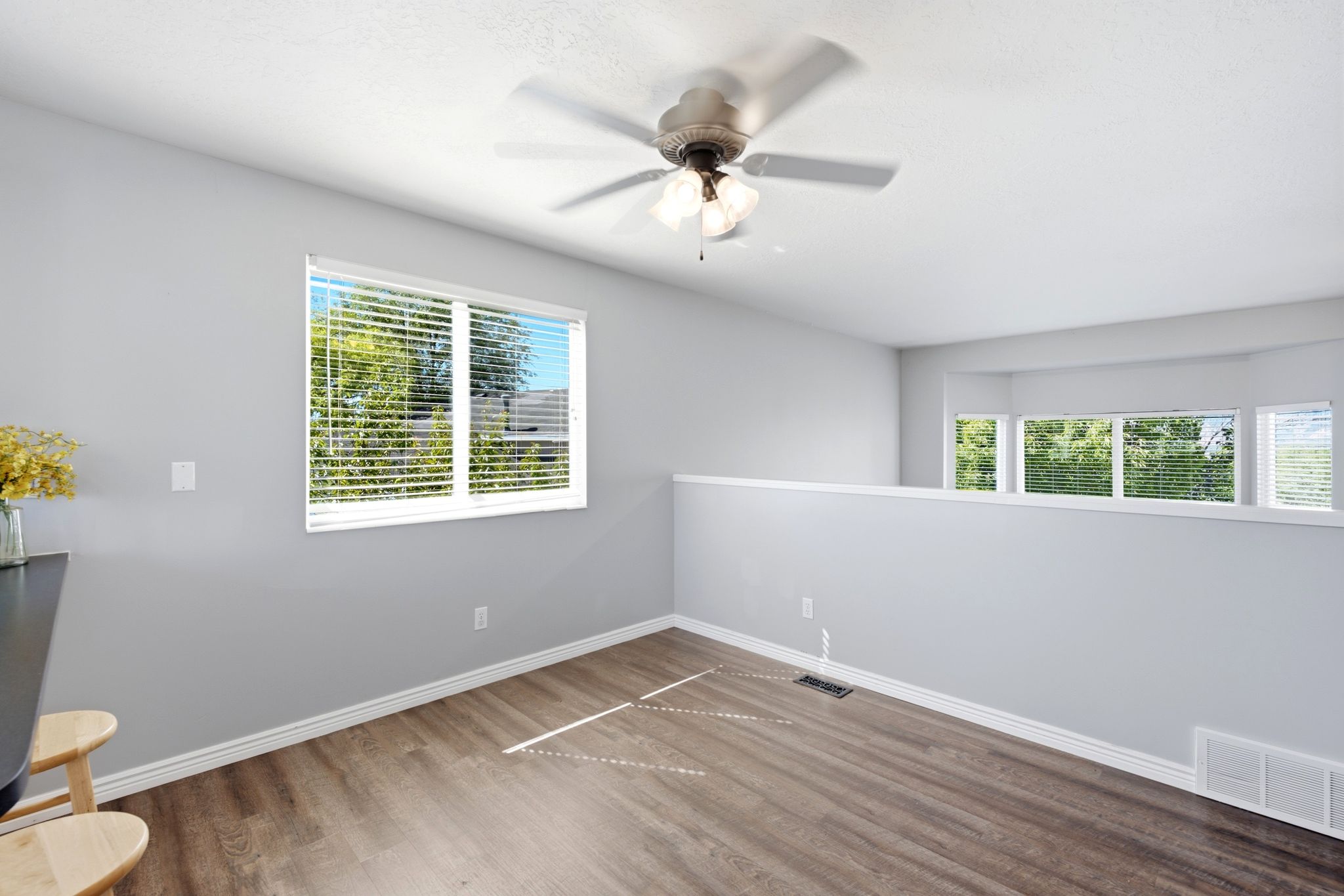 Bright interior space featuring wood-finish flooring, a contemporary ceiling fan with integrated lighting, and multiple windows with white blinds