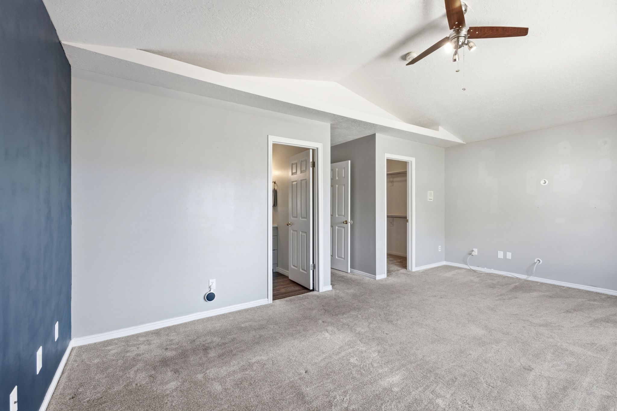 Spacious interior room featuring a tray ceiling, ceiling fan with wood-finish blades, and neutral gray carpeting