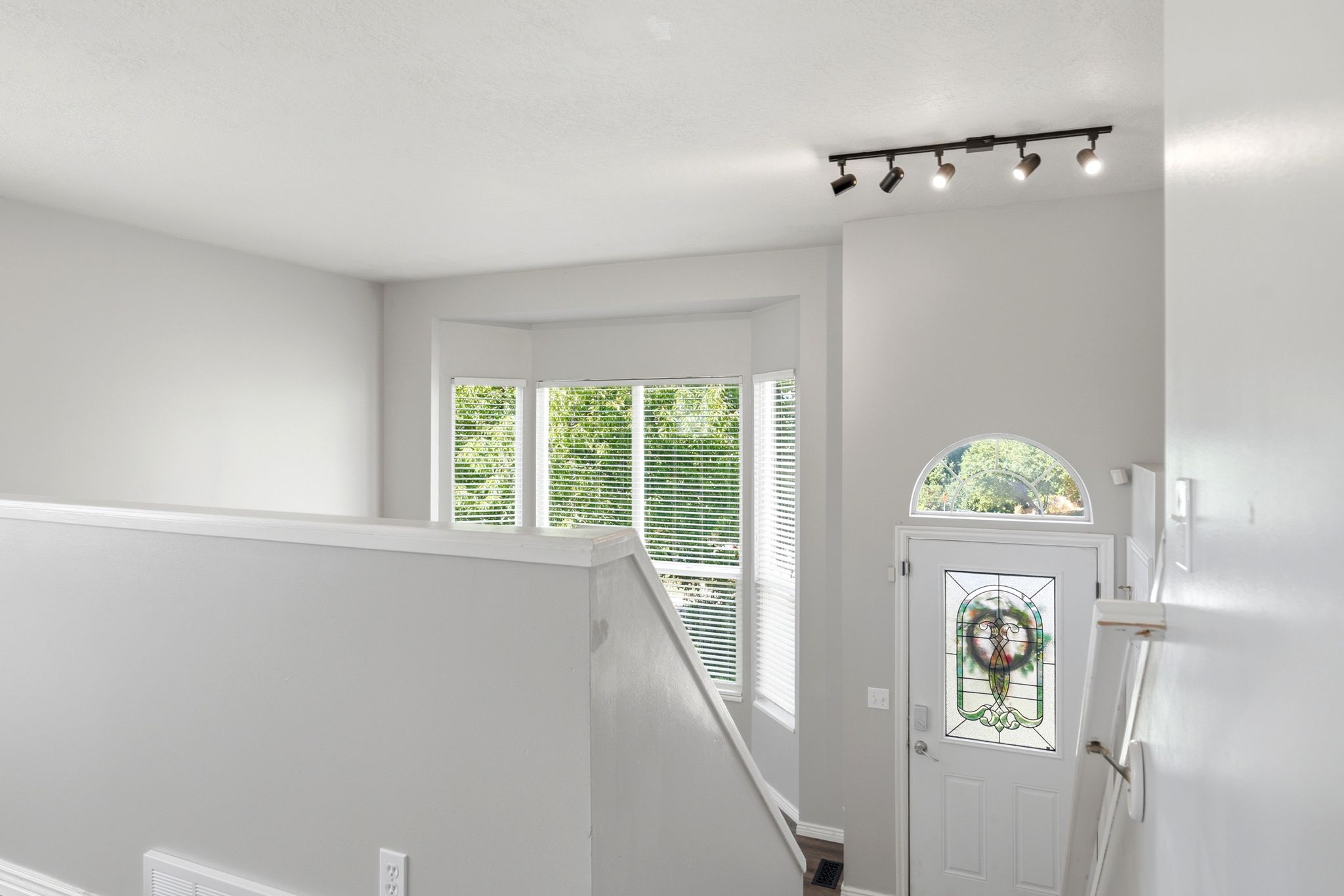 Entryway featuring a white door with a leaded glass insert, an arched transom window, and track lighting