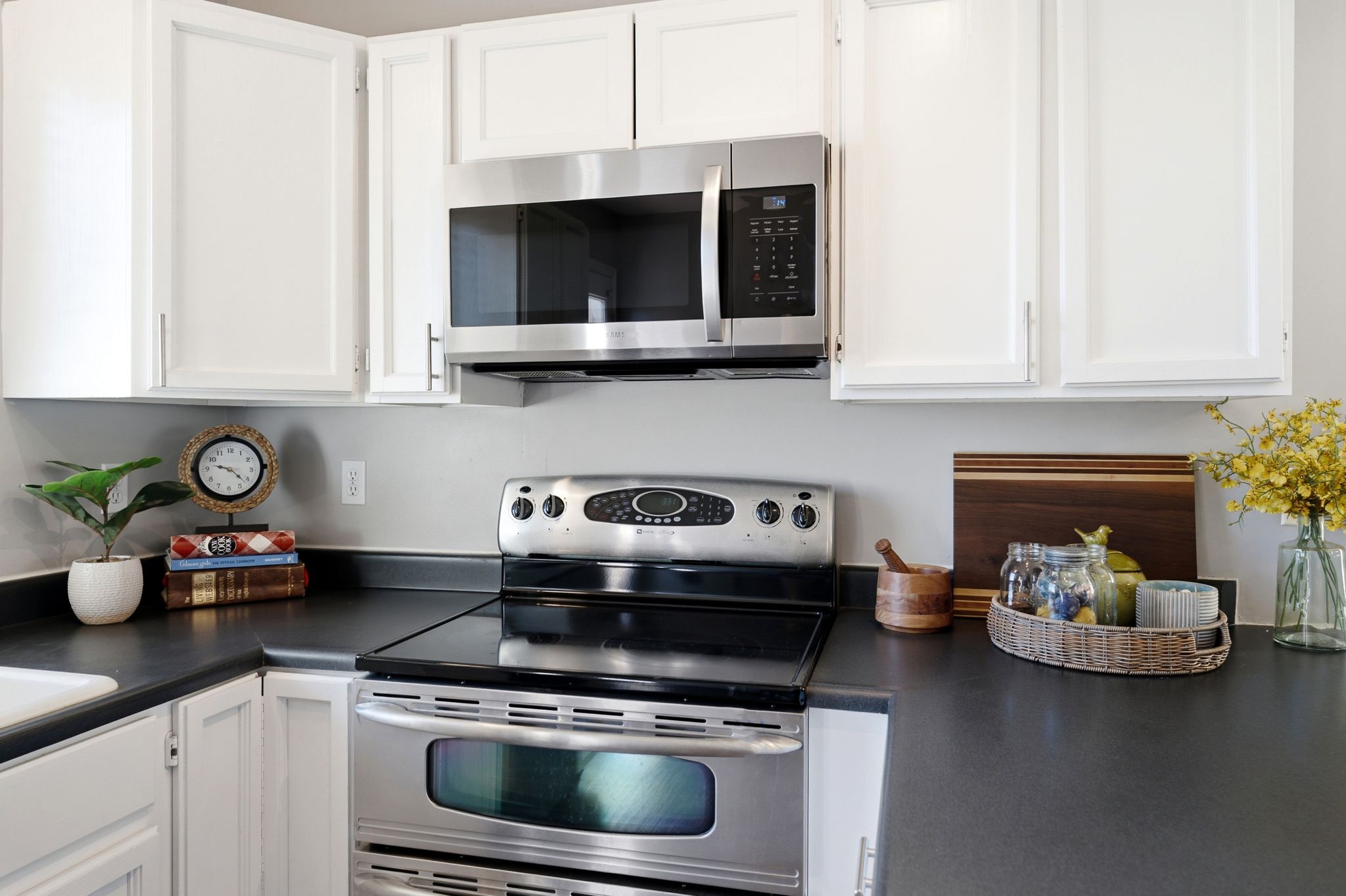 Kitchen featuring white cabinetry with silver-tone hardware, dark countertops, and stainless steel appliances including an oven with a ceramic cooktop and an over-the-range microwave