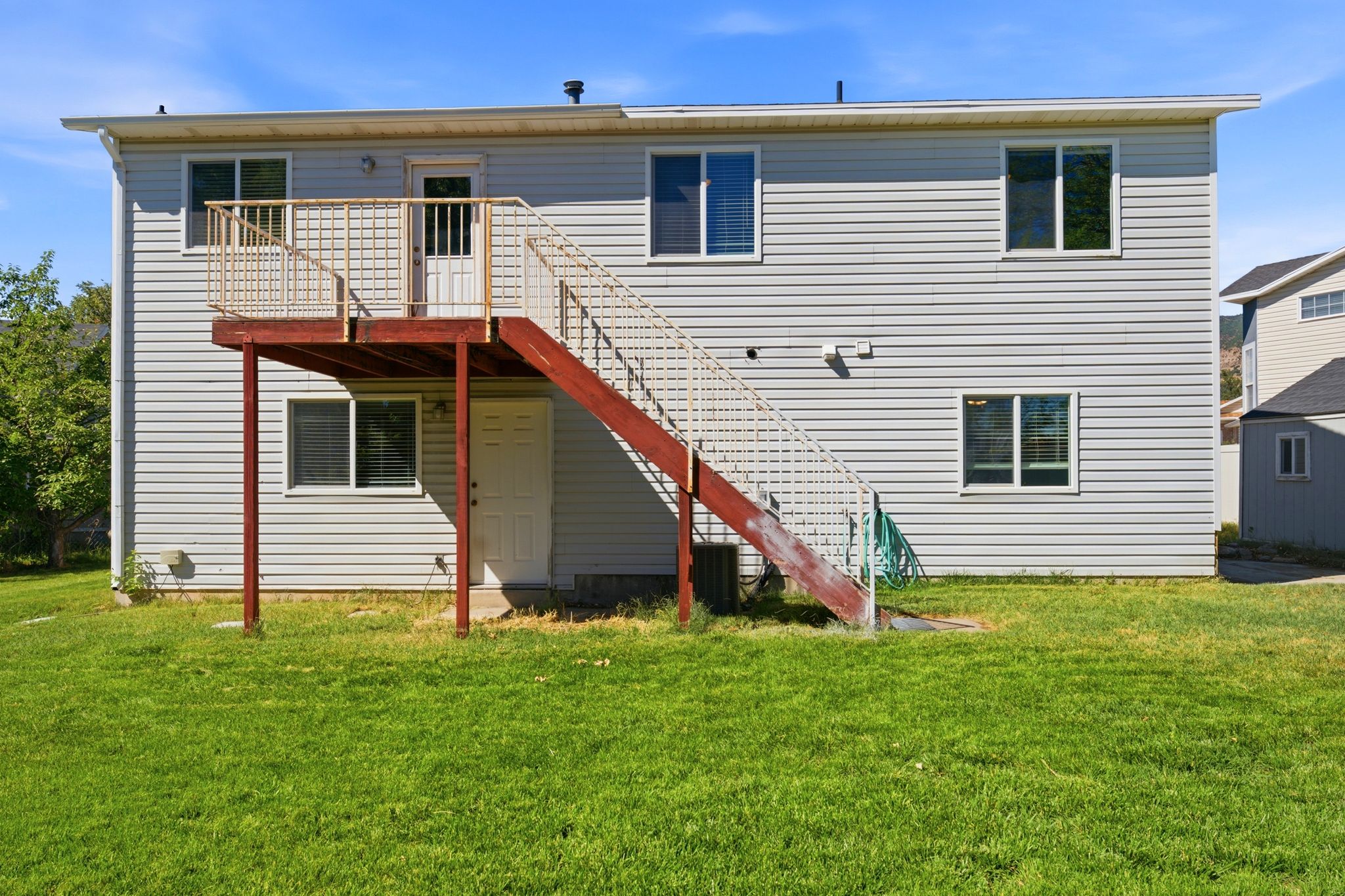 Rear exterior featuring light-colored siding, a second-story deck with a metal railing, and an exterior staircase providing access to the ground level
