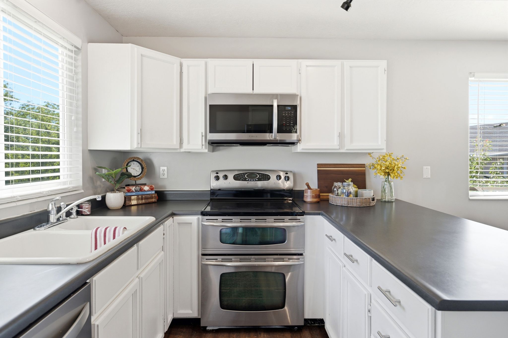 Kitchen featuring white cabinetry, dark countertops, stainless steel double oven range, stainless steel microwave, and white double basin sink