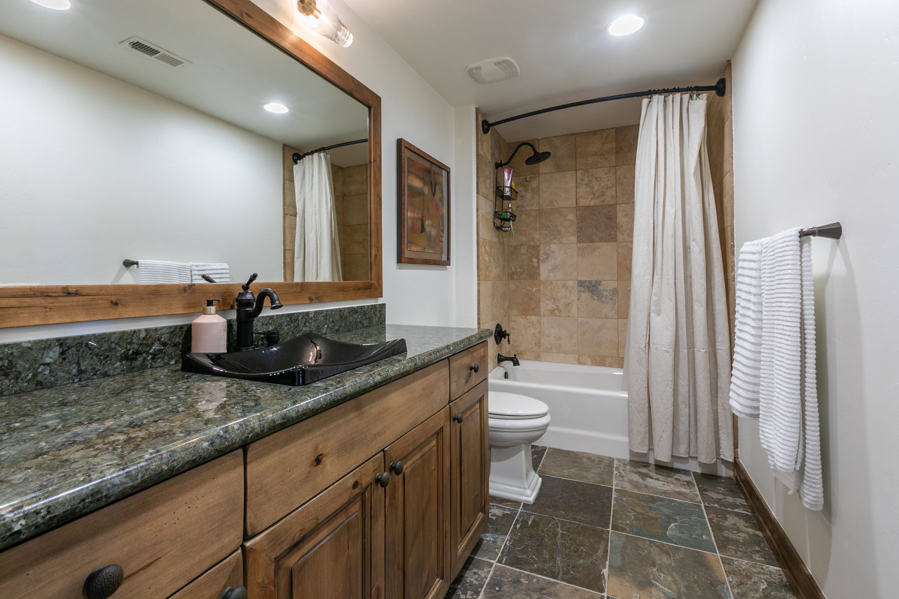 Bathroom featuring a wood-finish vanity with a dark countertop and a black vessel sink