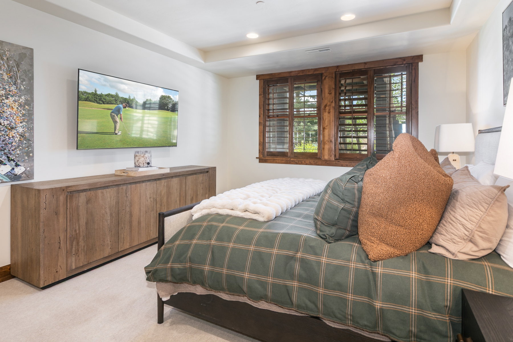 Recessed lighting illuminates this room, featuring a wall-mounted television above a wood-finish console