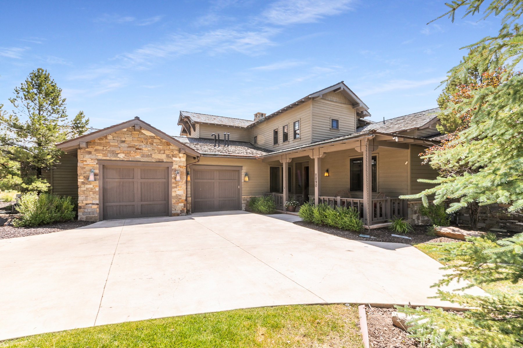 Craftsman-style residence featuring a prominent stone facade, two attached garage bays with wood-finish doors, and a covered front porch with a wood railing