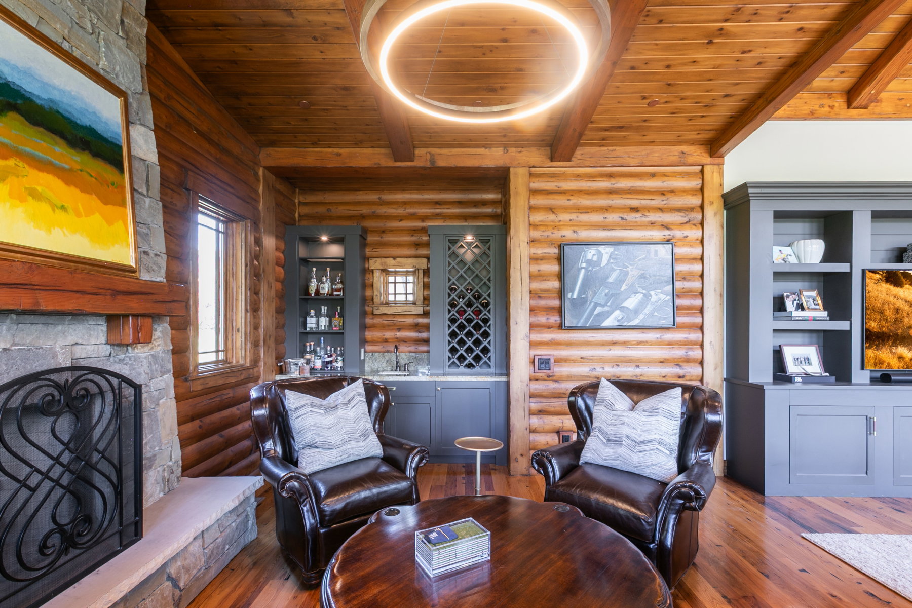 Wood-finish flooring and log walls define this space, featuring a stone fireplace with a decorative screen