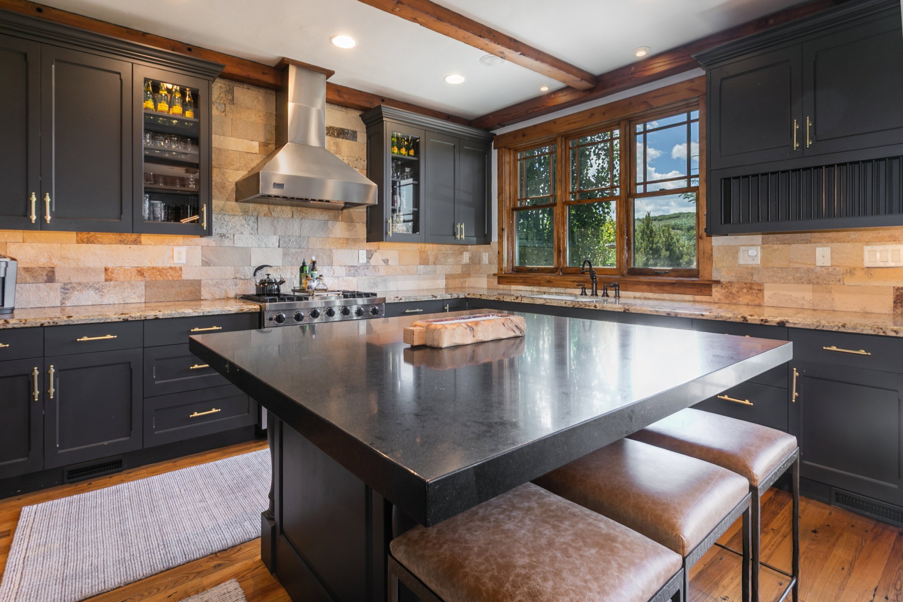 Spacious kitchen featuring dark cabinetry with gold-toned hardware, stone backsplash, granite countertops, and a central island with a dark countertop
