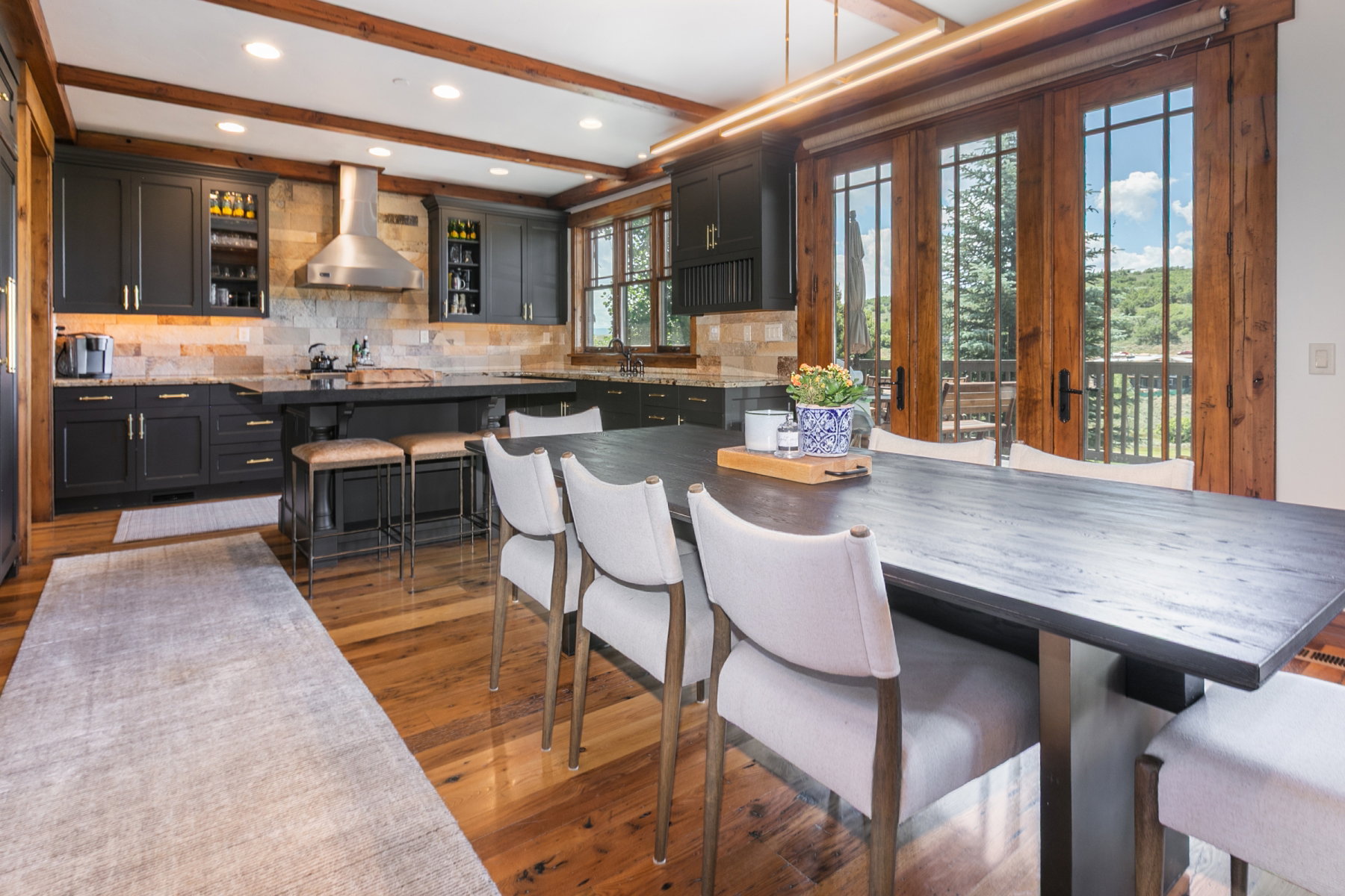 Spacious kitchen featuring dark cabinetry, stone tile backsplash, stainless steel range hood, wood-finish flooring, and multi-pane wood French doors