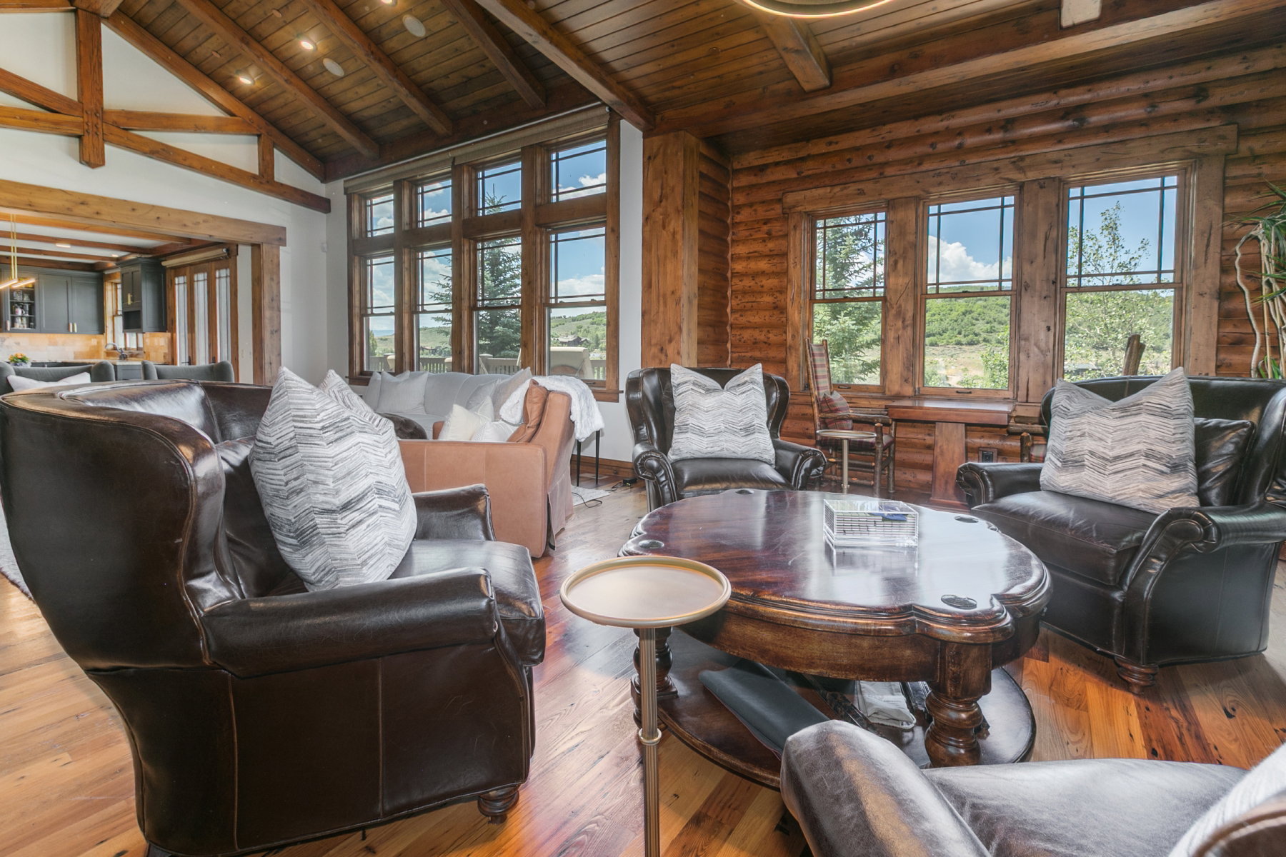 Living area featuring vaulted wood-plank ceilings with exposed beams, wood-finish flooring, a log wall with large windows, and a built-in recessed lighting fixture