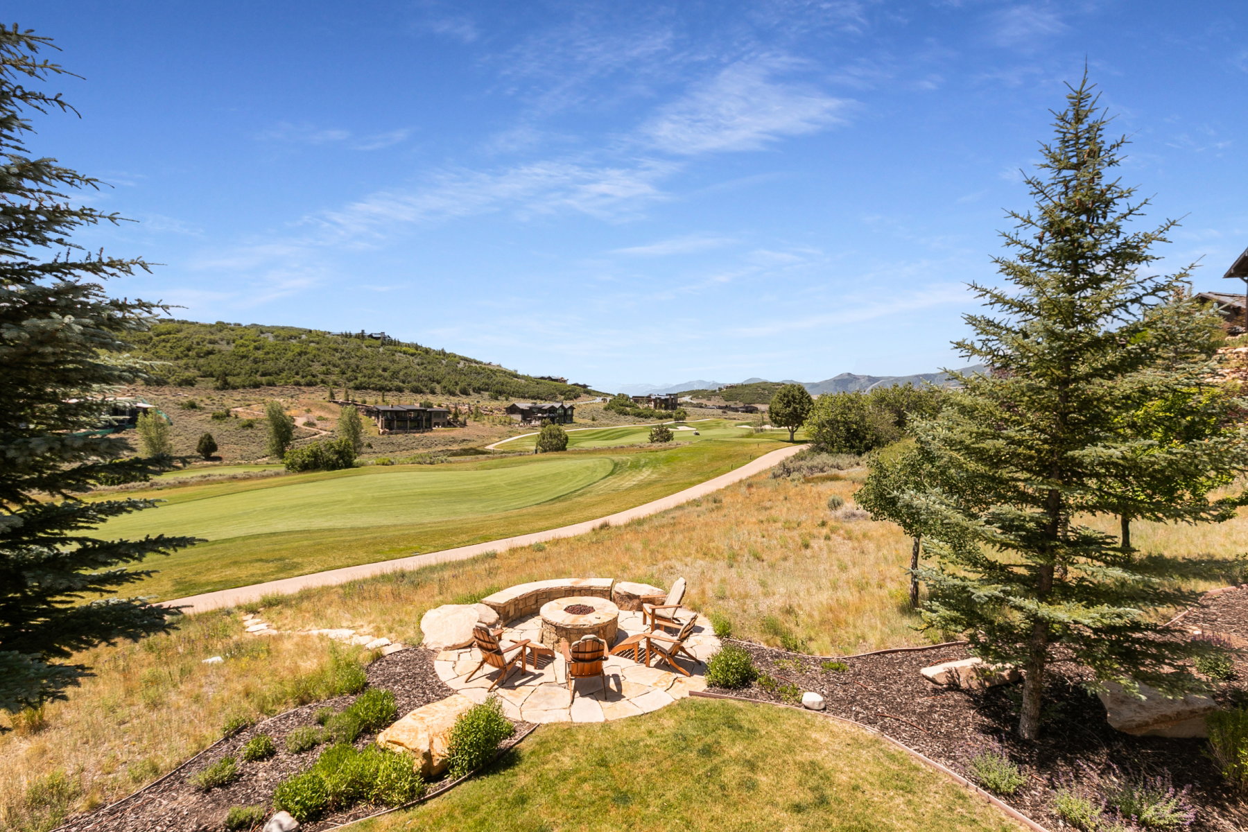 Stone patio featuring a built-in fire pit, surrounded by a landscaped yard with established trees