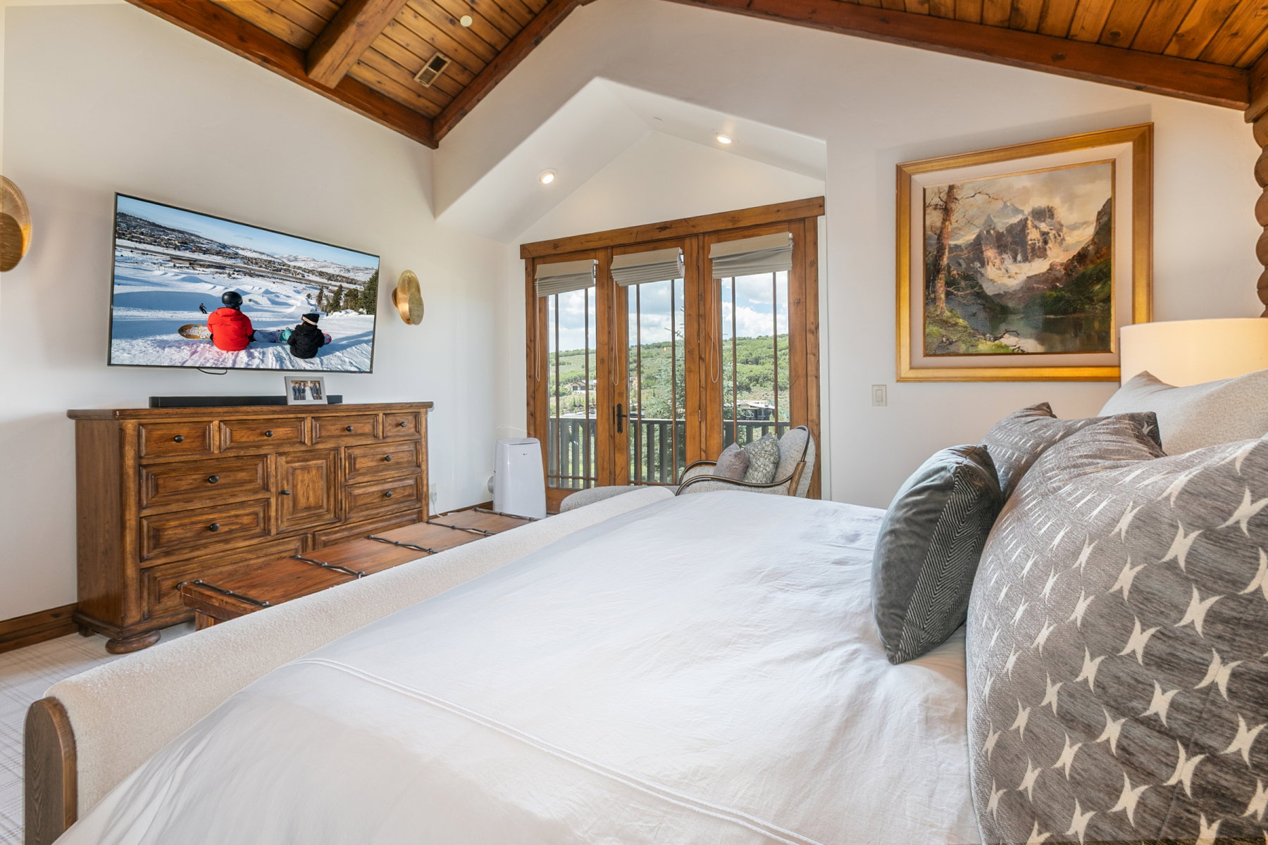 Vaulted wood-plank ceilings with exposed beams, light walls, and wood-frame double doors opening to an exterior balcony