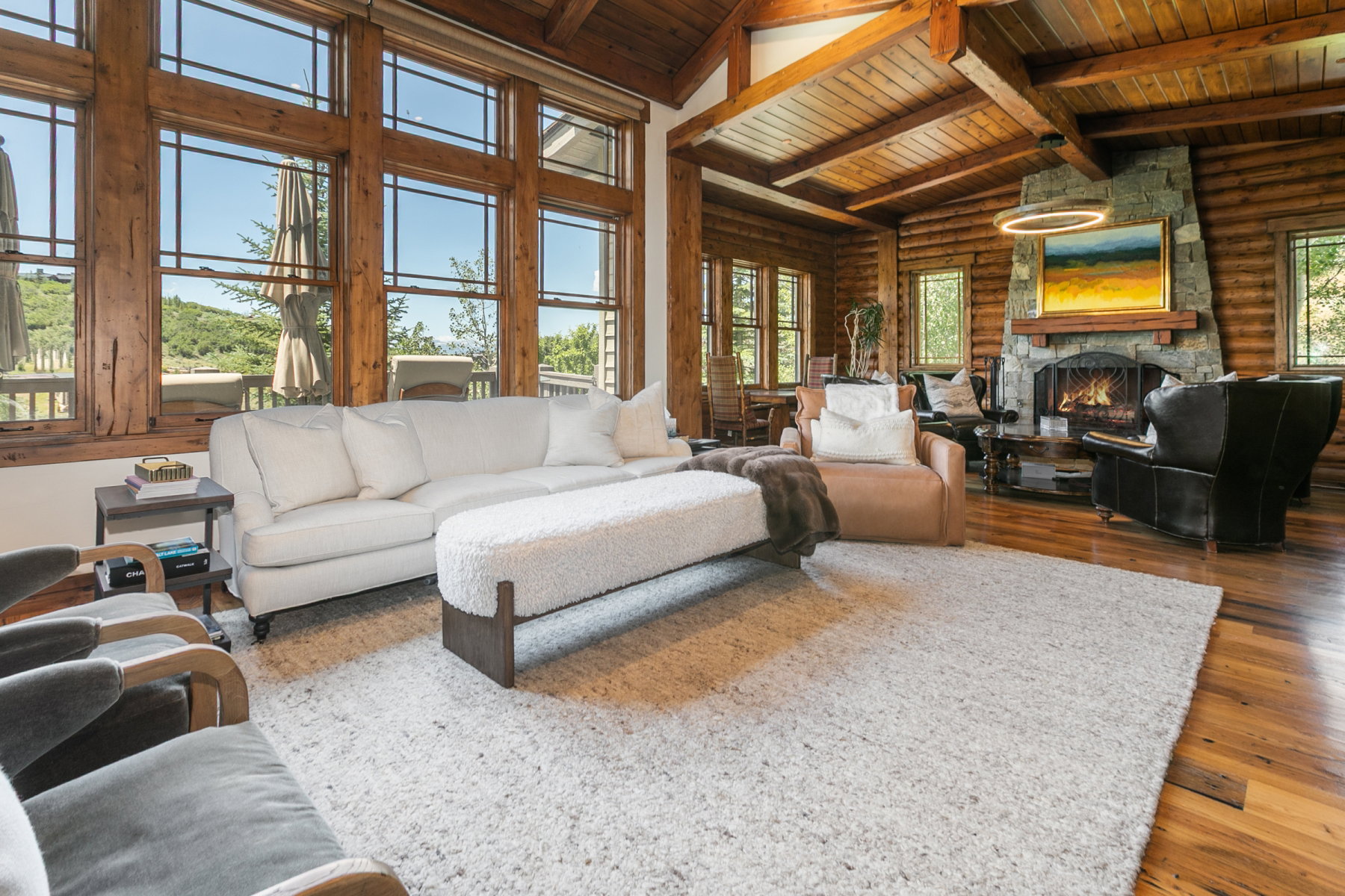 Spacious living area featuring expansive wood-framed windows, a prominent stone fireplace, and wood-finish flooring