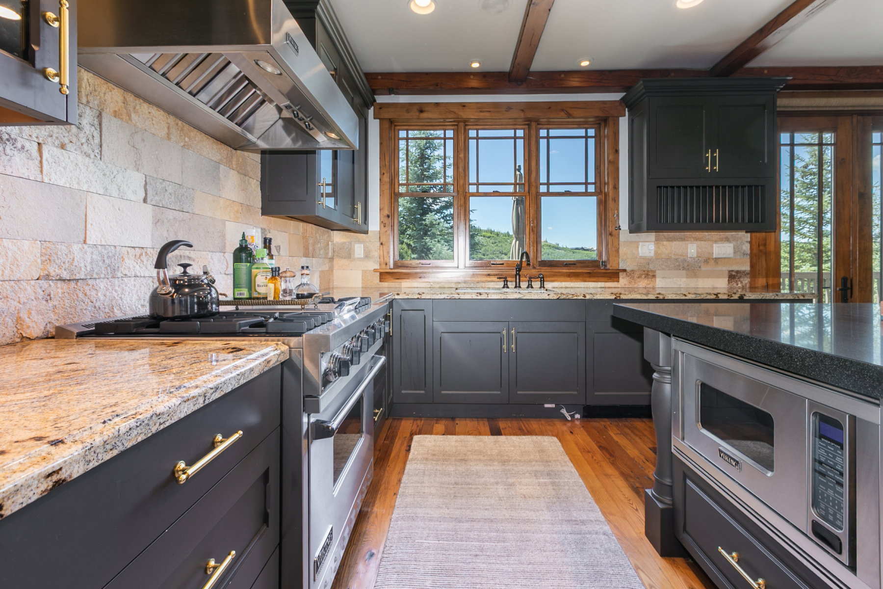 Well-appointed kitchen featuring granite countertops, stainless steel appliances, a stone tile backsplash, and exposed wood ceiling beams