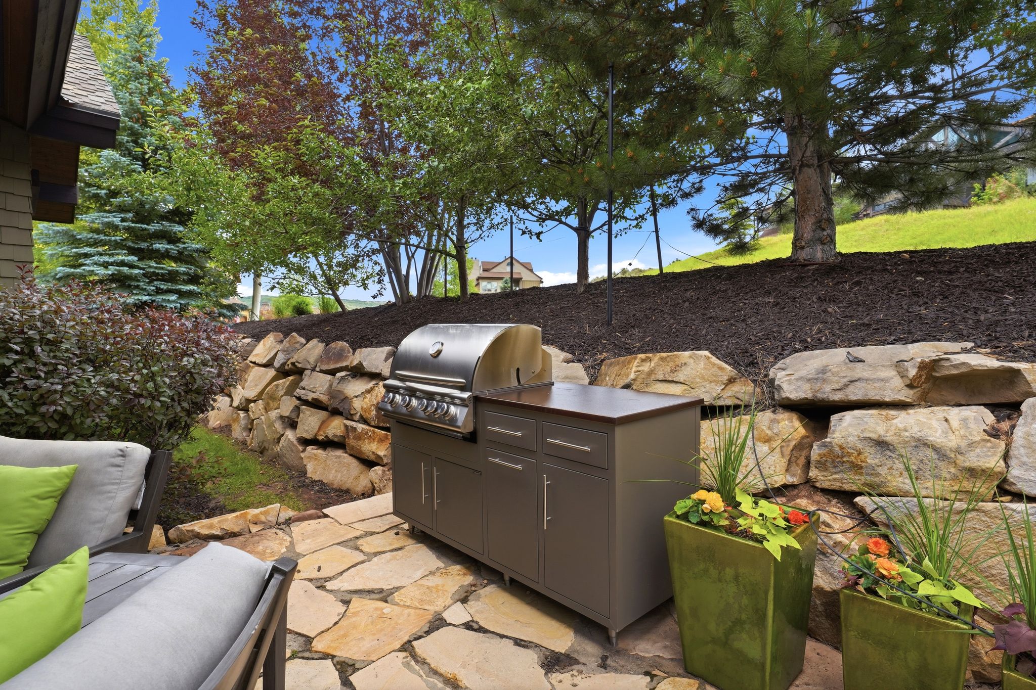 Outdoor entertainment area featuring a flagstone patio, built-in grill with cabinetry, tiered landscaping, and natural stone retaining walls