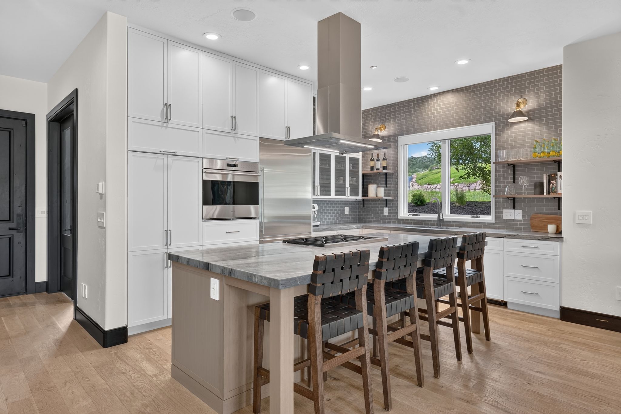Gourmet kitchen featuring a large central island with seating, integrated stainless steel appliances, light wood-finish flooring, full-height white cabinetry, and a grey brick-patterned backsplash