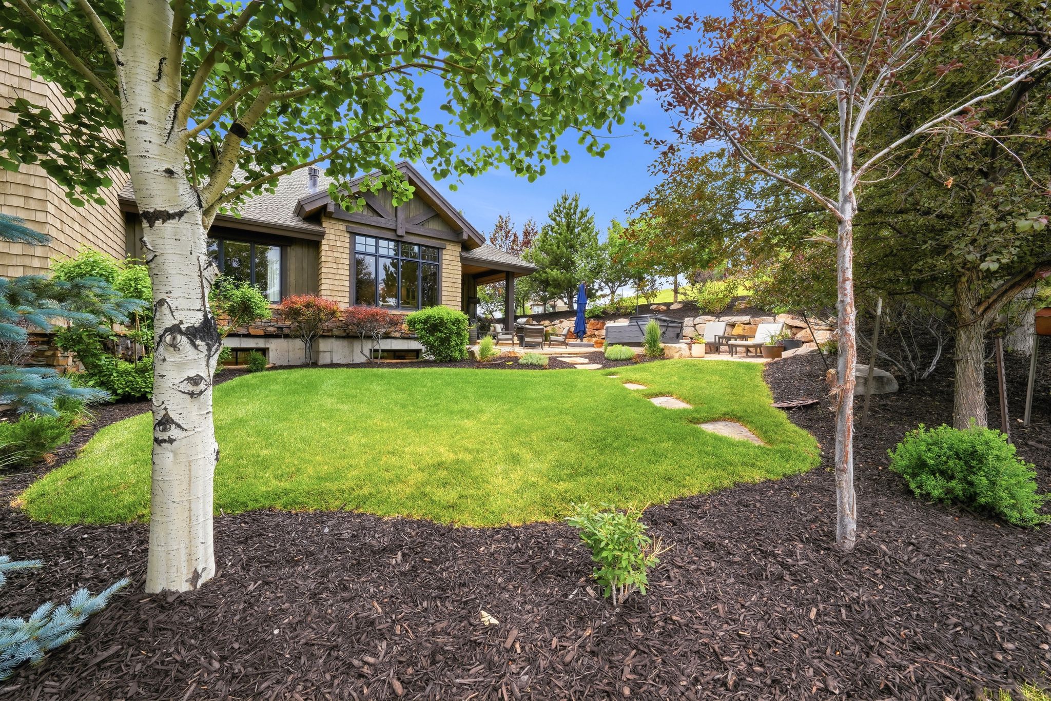 Spacious backyard featuring a manicured lawn, stone paver pathway, and mature trees