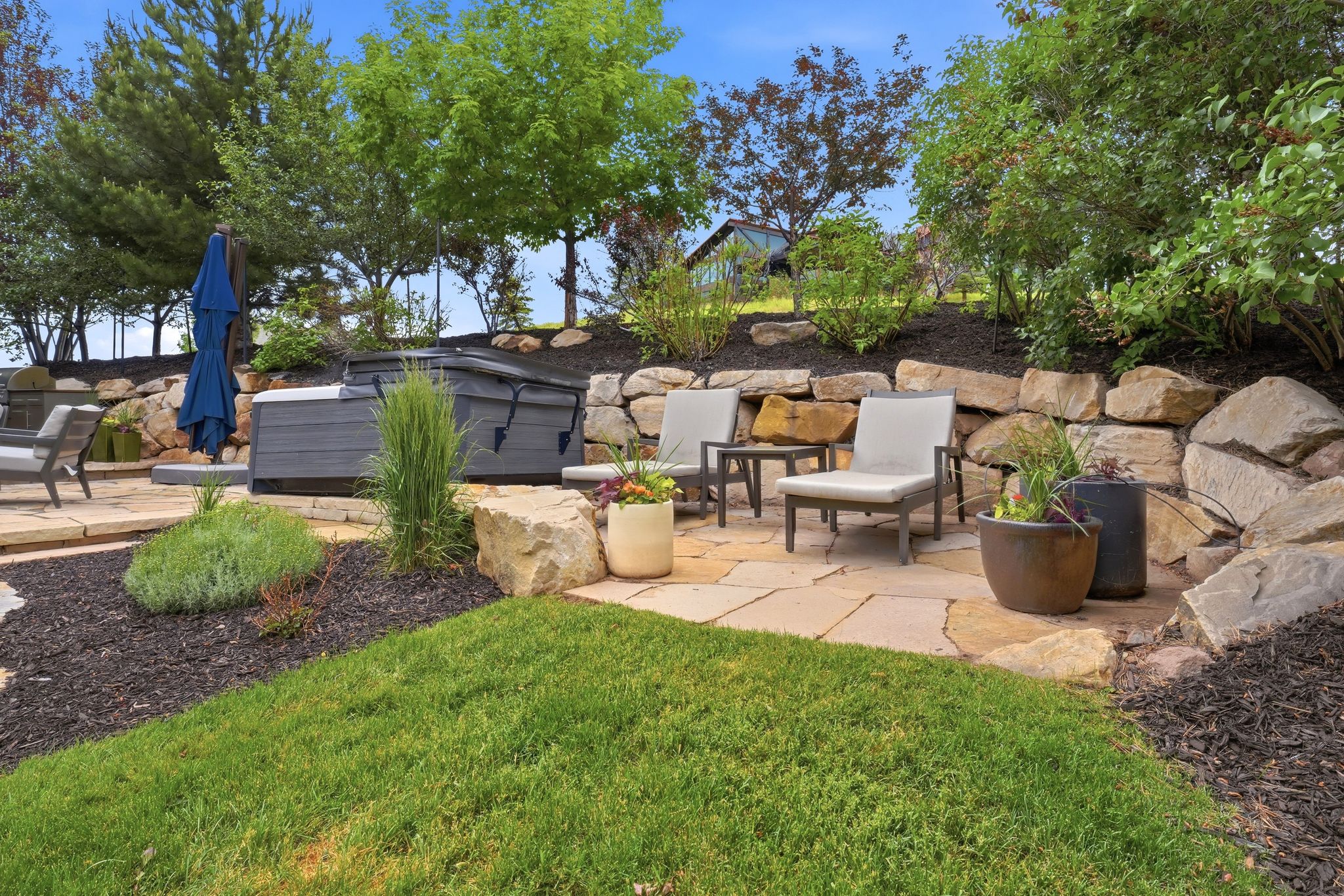 Flagstone patio area featuring a built-in hot tub, natural rock retaining wall, and mature landscaping