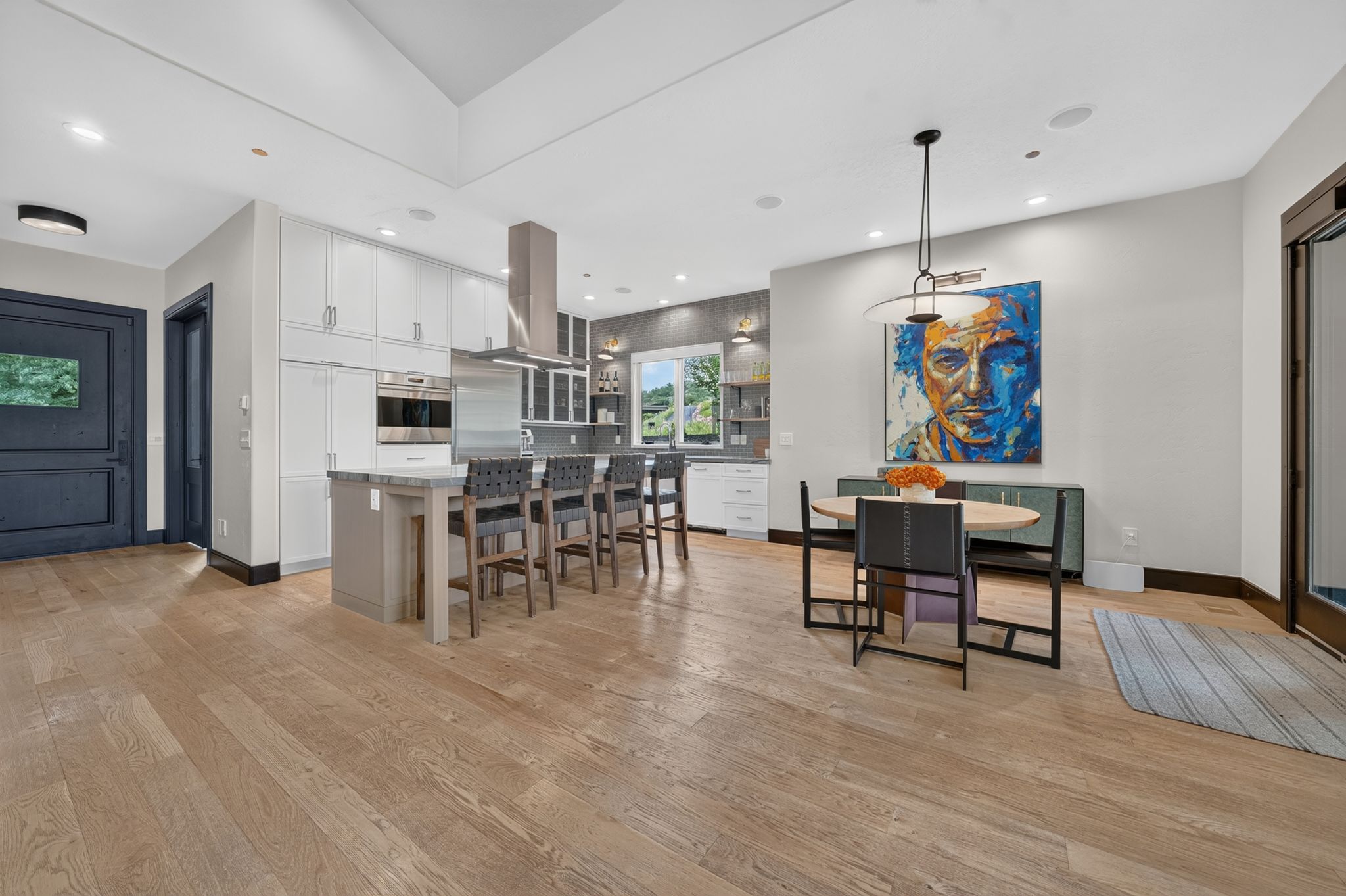 Open-concept living area featuring light wood-finish flooring, a large kitchen island with seating, white cabinetry, and stainless steel appliances