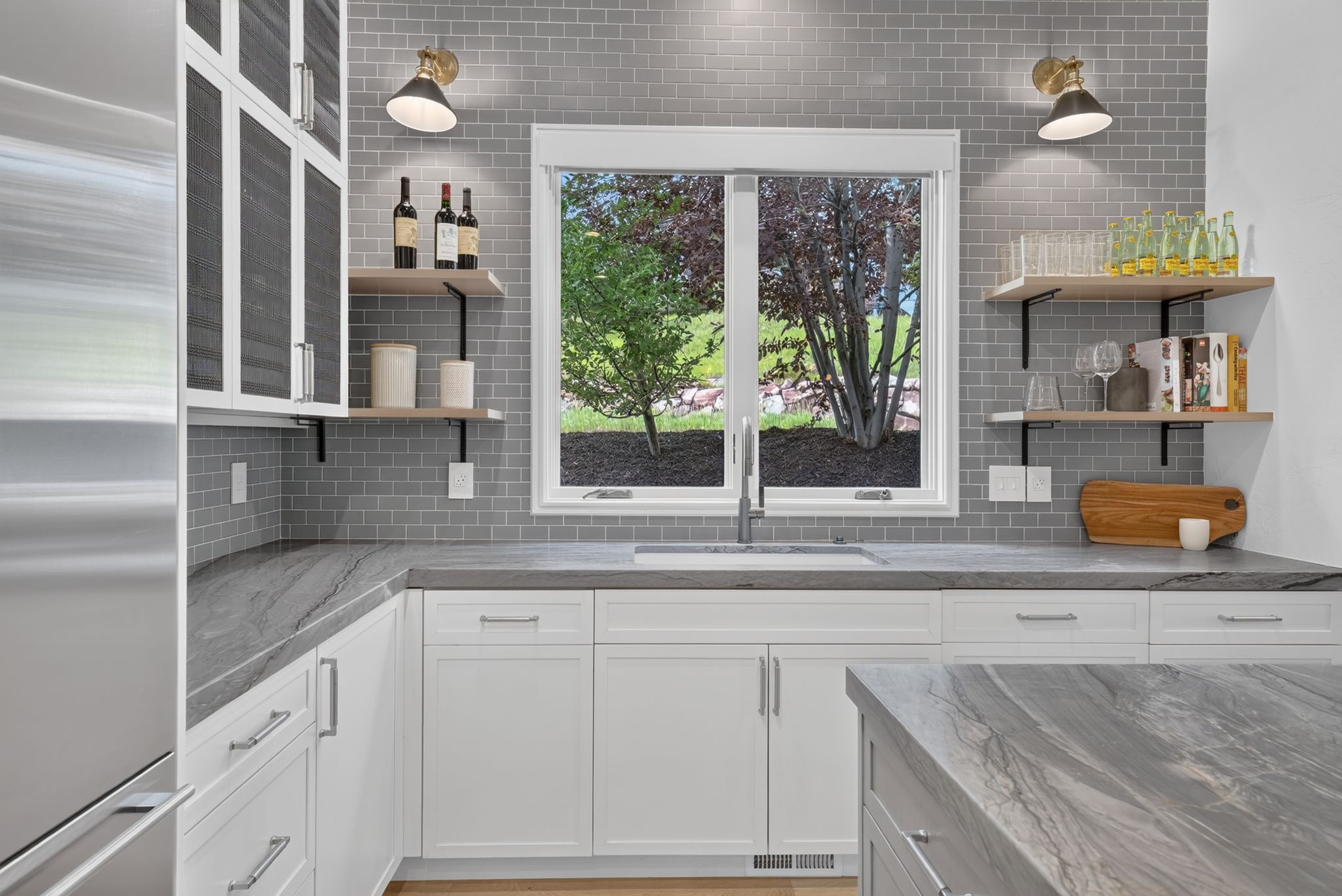 Kitchen with grey subway tile backsplash, white shaker cabinetry, stainless steel sink, and light wood-finish open shelving