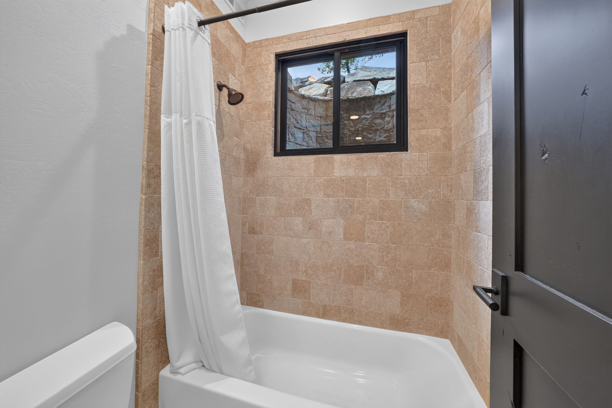 Tub-shower combination featuring textured tile surround, a built-in window, and a bronze-finish showerhead