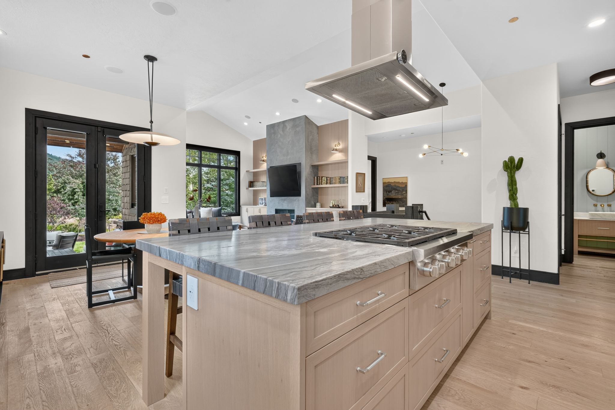Light wood-finish flooring complements this open-concept kitchen featuring an expansive center island with a built-in gas range and overhead stainless steel range hood