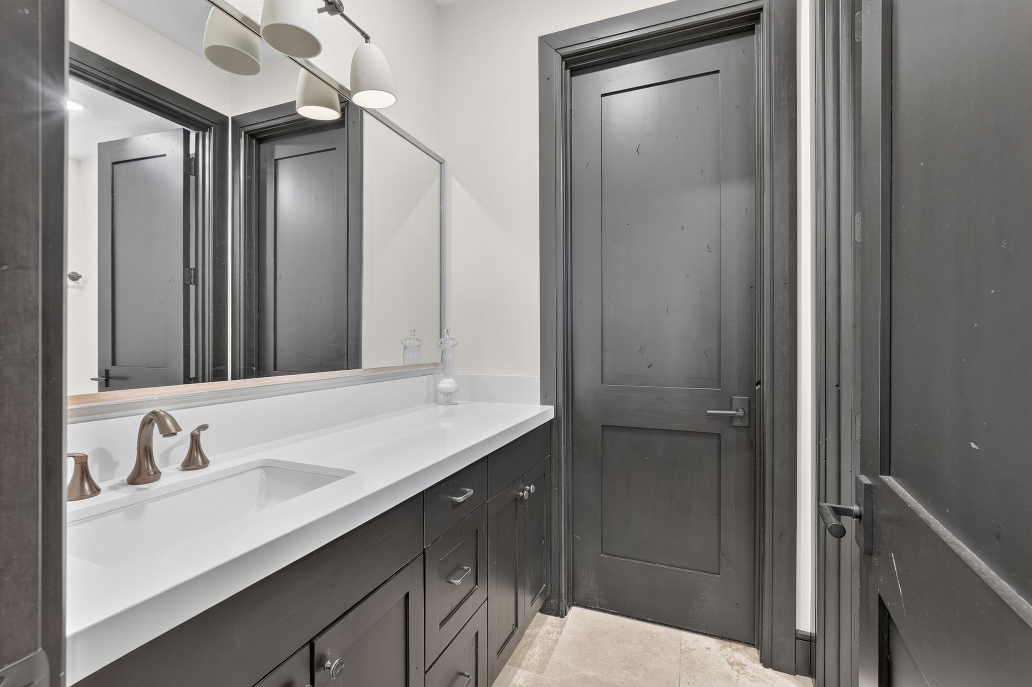 Bathroom vanity featuring a single integrated sink, white countertop, dark wood-finish cabinetry, and brushed bronze fixtures