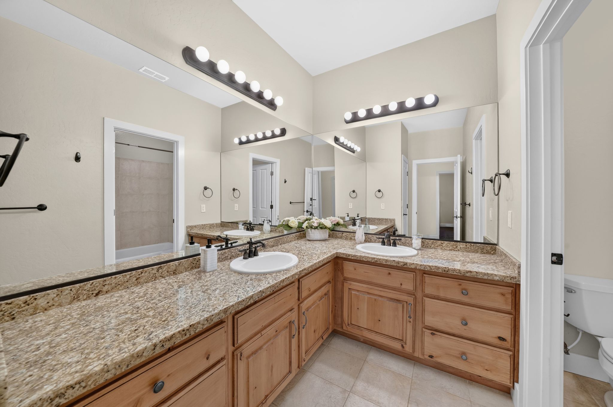 Dual vanity with light wood cabinetry, speckled countertops, and undermount sinks