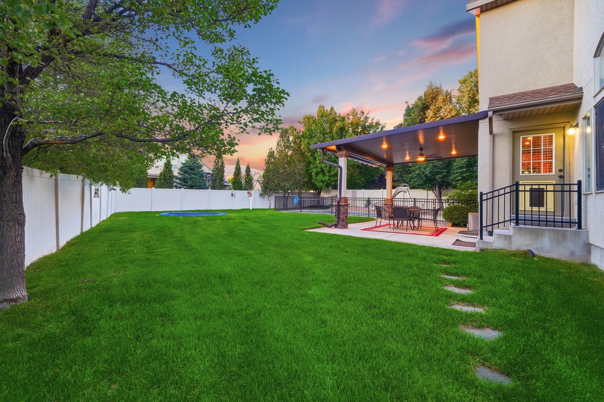 Expansive backyard featuring a lush lawn, white privacy fencing, and a concrete patio with an attached covered pergola