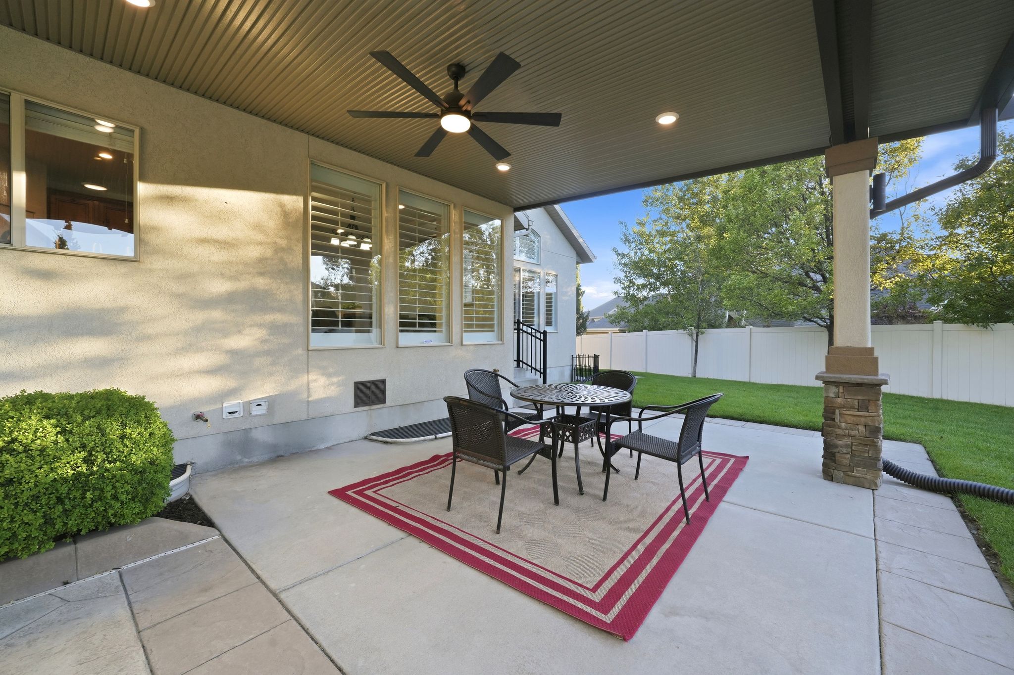 Covered patio with recessed lighting and a ceiling fan, featuring a concrete surface and a stone-clad support column
