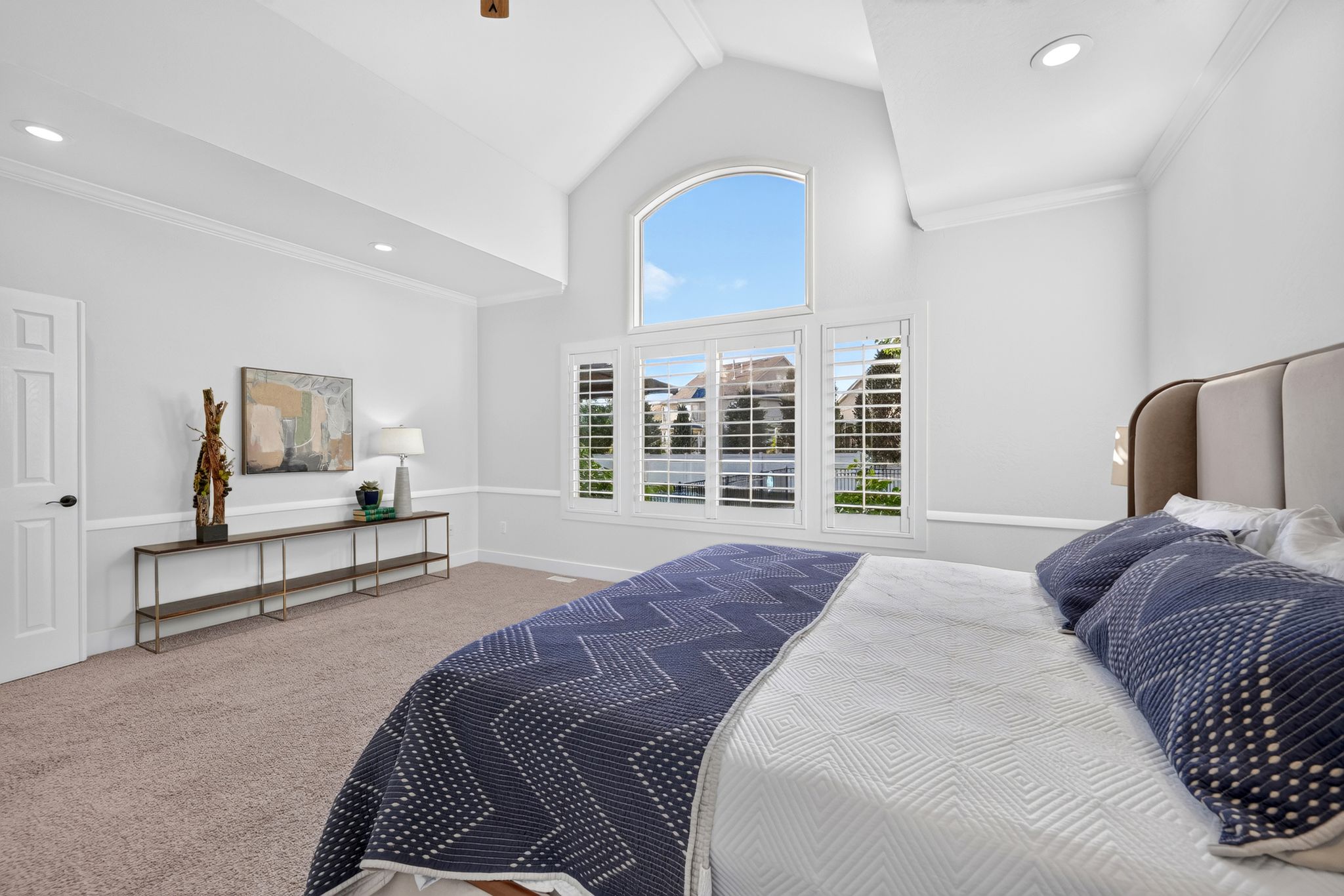 Vaulted ceiling bedroom featuring an arched window, plantation shutters, recessed lighting, and crown molding
