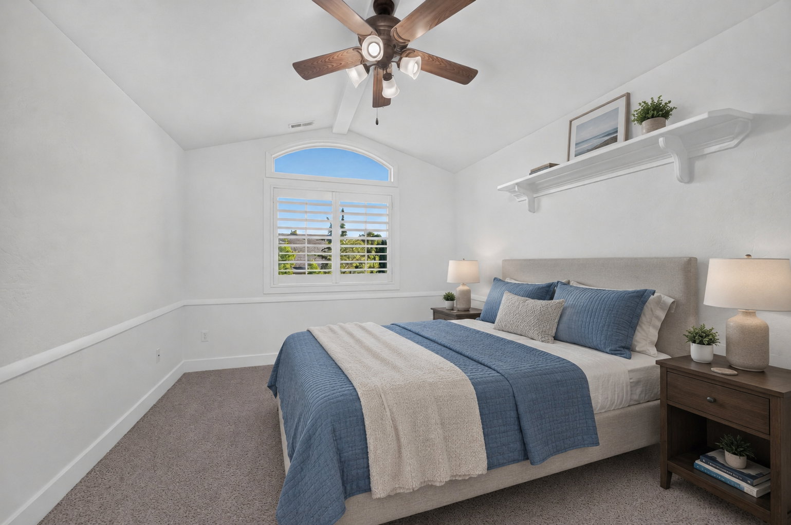 Carpeted bedroom featuring an arched window with white plantation shutters, a ceiling fan with integrated lighting, and a white wall-mounted shelf