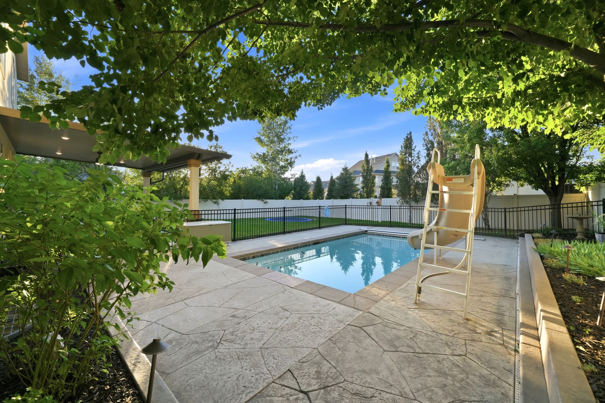 Outdoor swimming pool with patterned concrete decking, surrounded by mature trees and lush landscaping