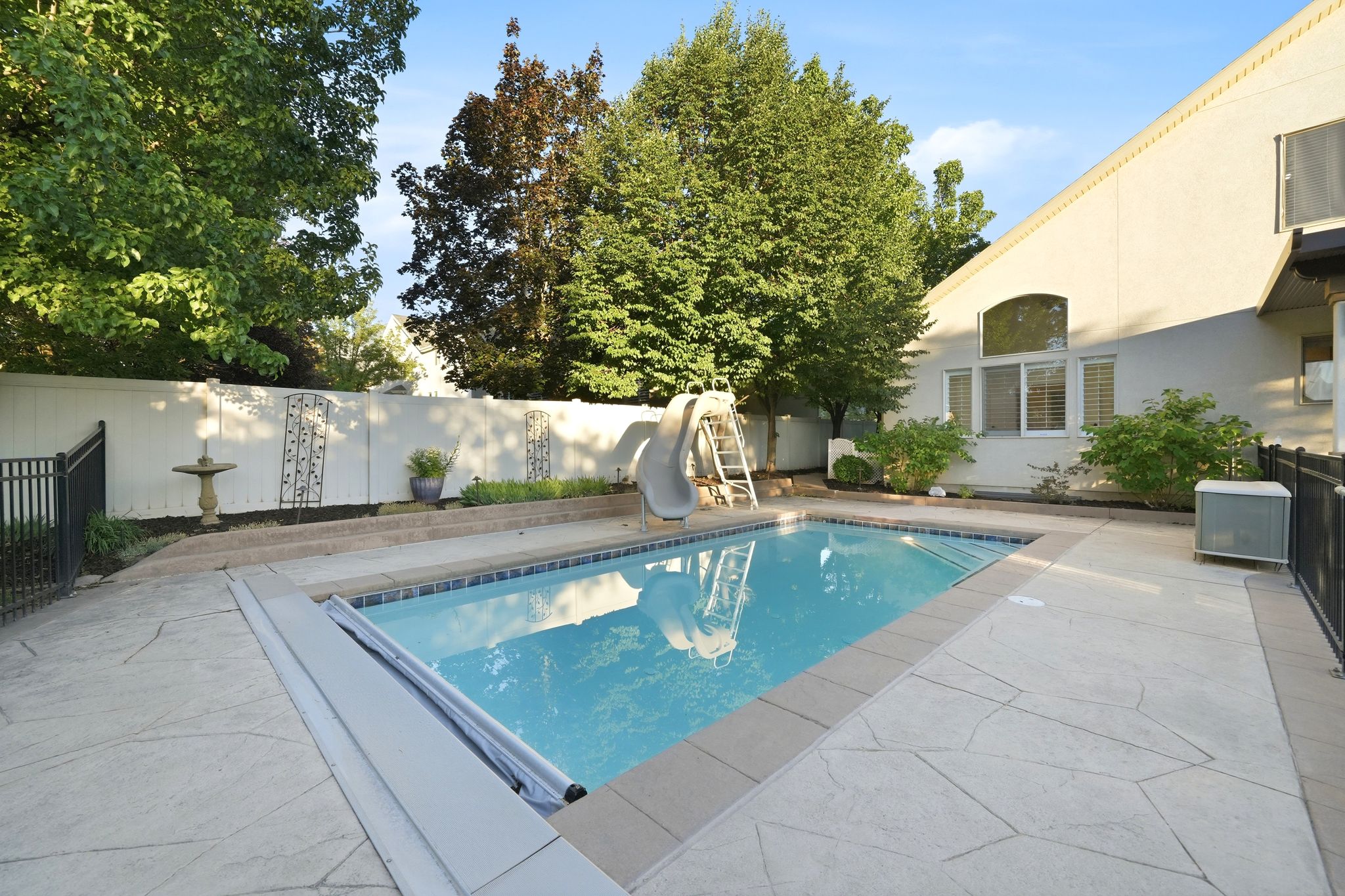 In-ground swimming pool featuring a retractable cover, bordered by stamped concrete paving and a privacy fence