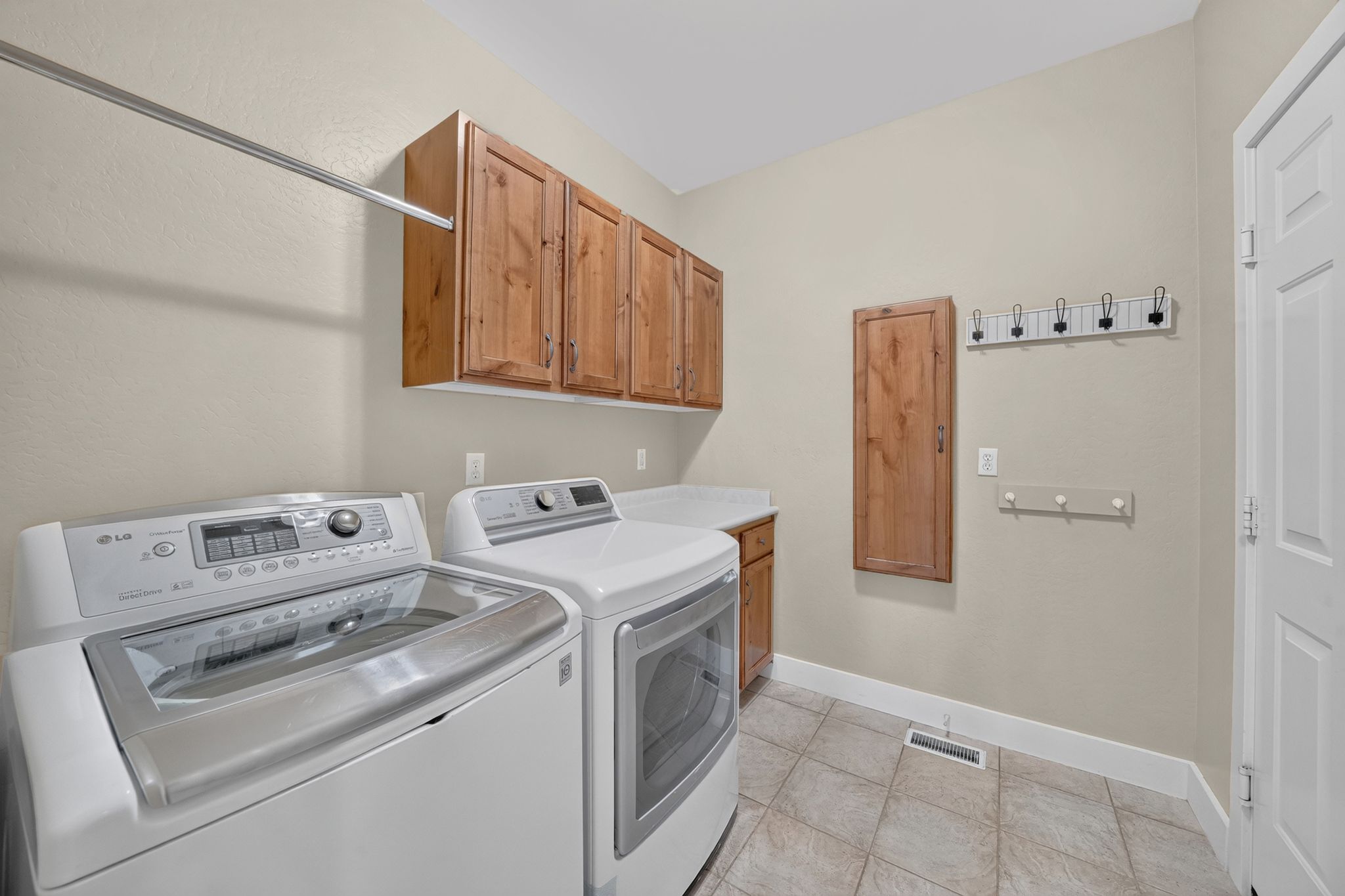 Utility room featuring wood cabinetry, a white countertop, ceramic tile flooring, and a metal hanging rod