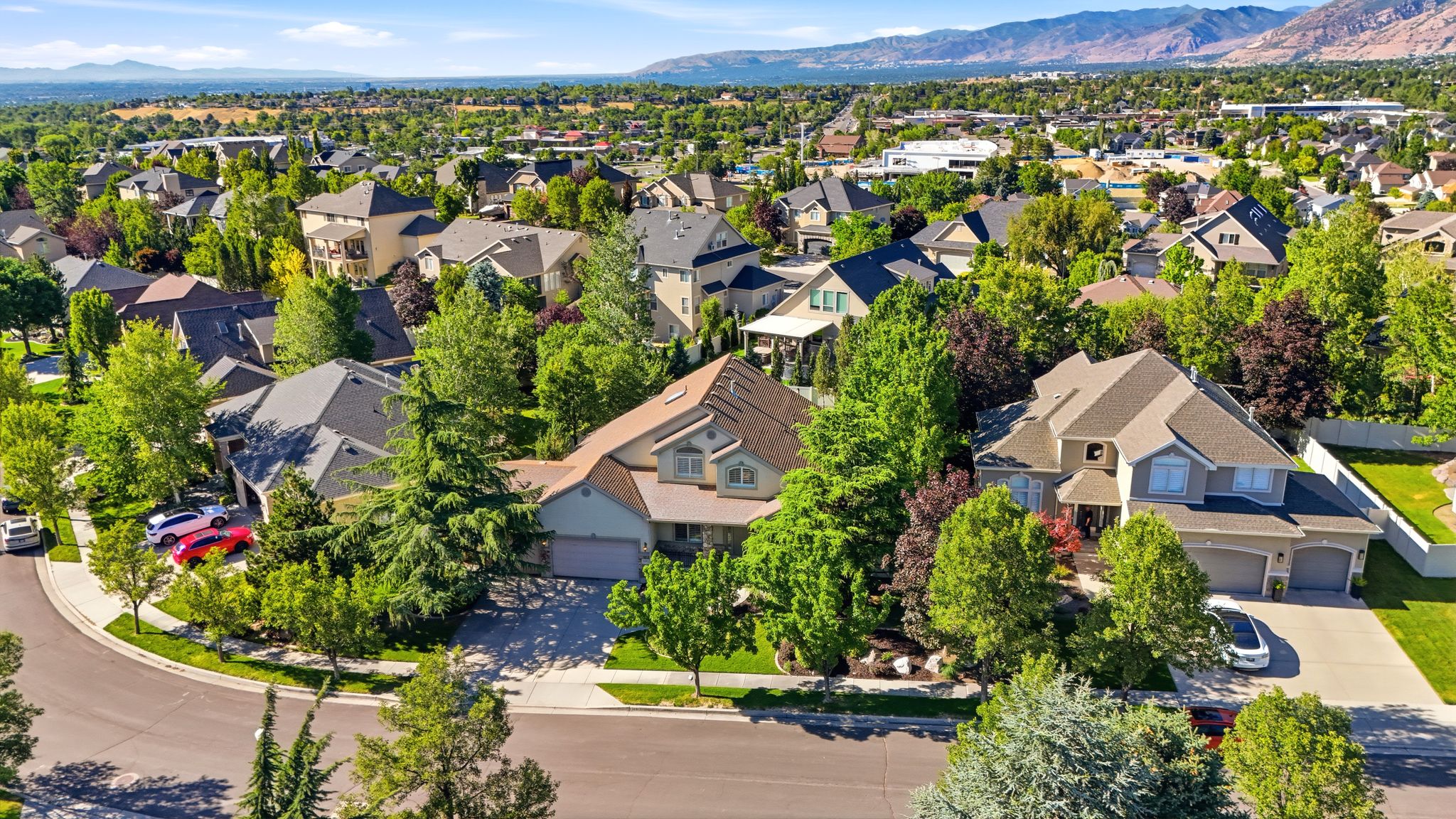 Residential streetscape featuring a curved road, concrete sidewalks, and mature landscaping