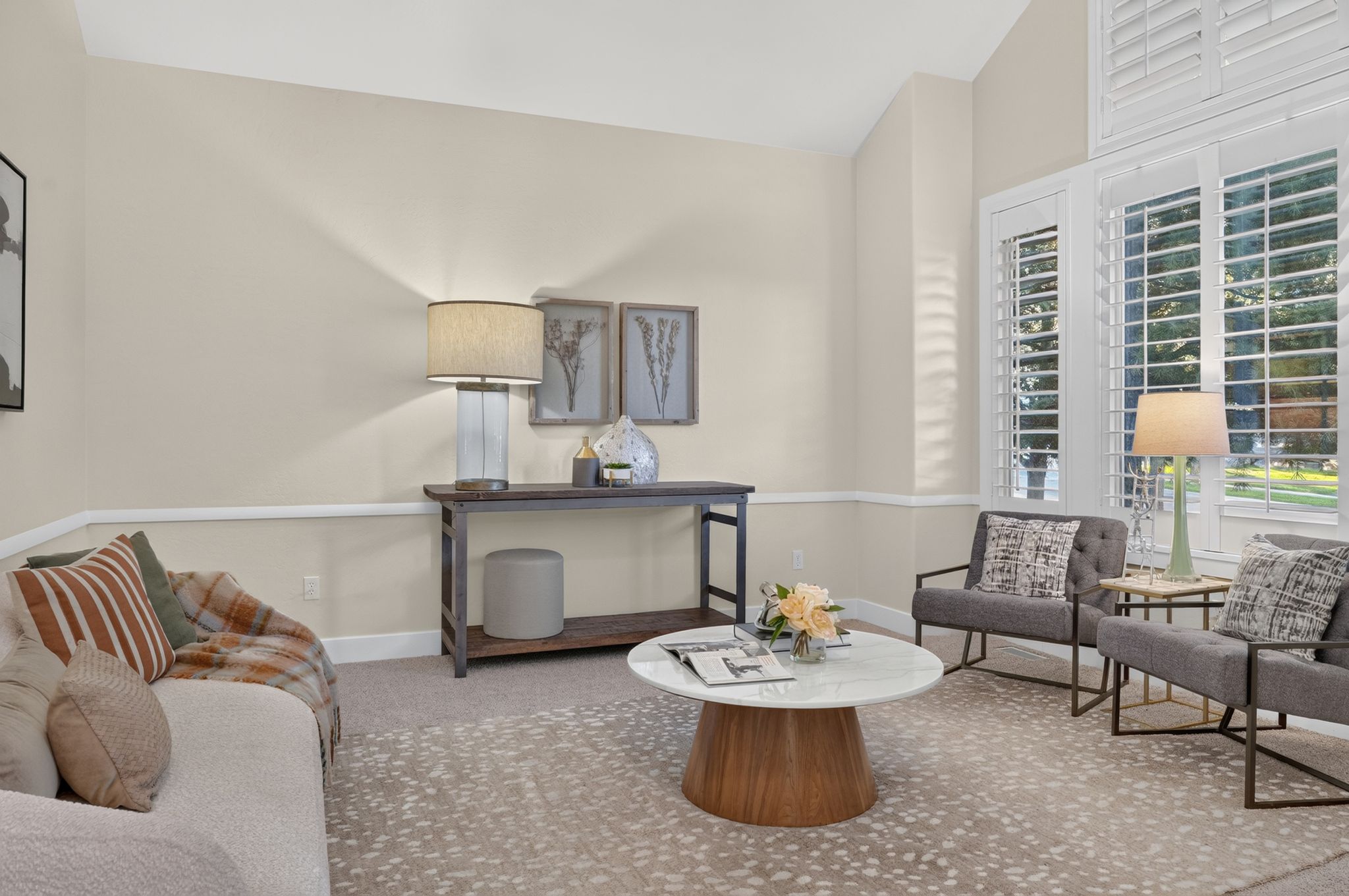 Spacious living area featuring neutral wall tones, white crown molding, and large windows with plantation shutters